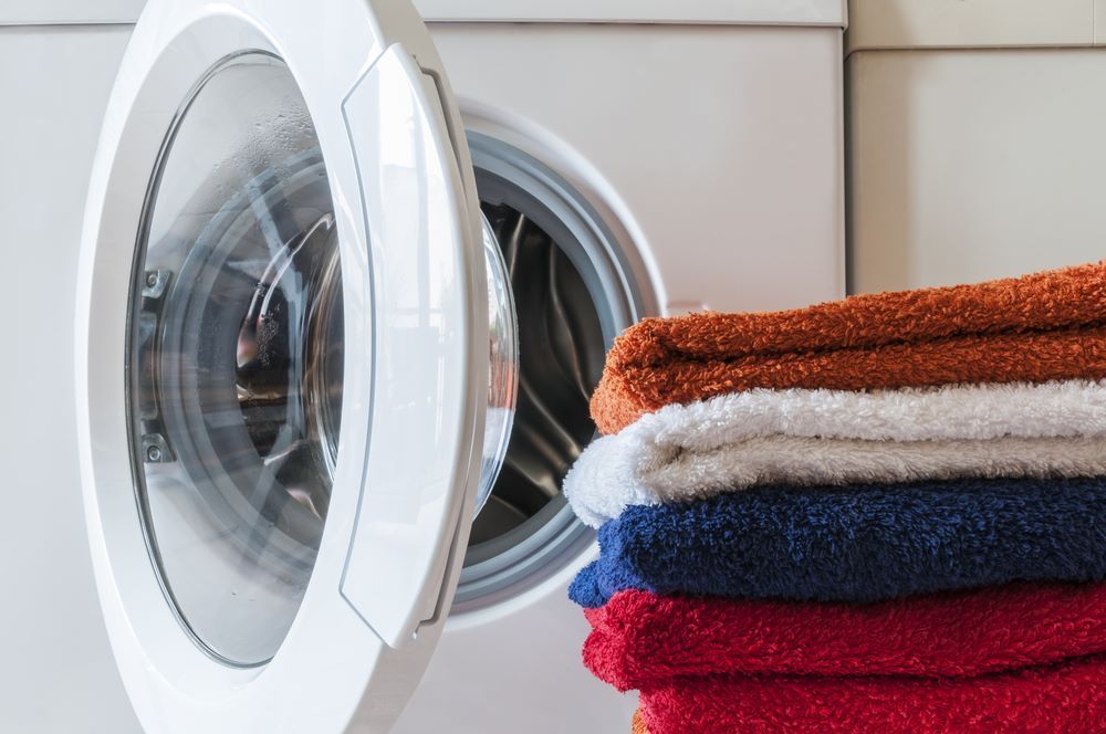 A Stack of Towels is Sitting Next to a Washing Machine — Super Suds Commercial Laundry in Avoca, QLD