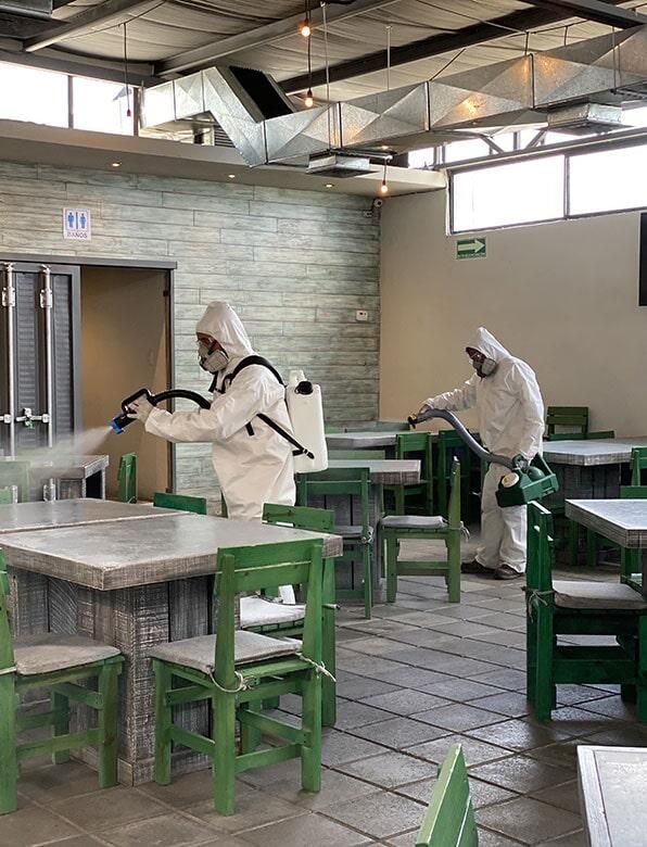 Dos hombres están desinfectando mesas y sillas en un restaurante.