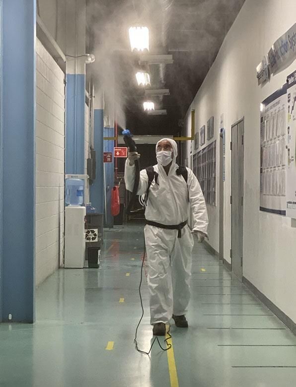 Un hombre con traje de protección está rociando desinfectante en un pasillo.