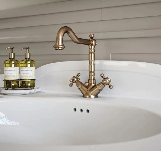 Un lavandino del bagno con un rubinetto in ottone e due bottiglie di sapone per le mani
