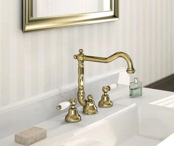 Un lavandino del bagno con rubinetto dorato e maniglie bianche