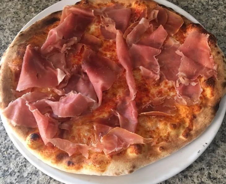 Una pizza con prosciutto sopra è su un piatto bianco