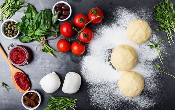 Un tavolo ricoperto di pasta, pomodori, mozzarella, olive e altri ingredienti per la pizza.