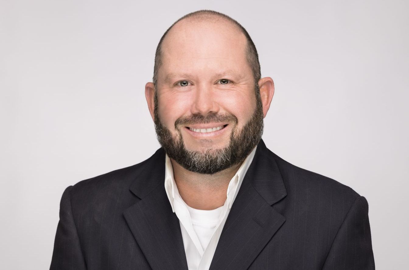 A bald man with a beard is wearing a suit and smiling.
