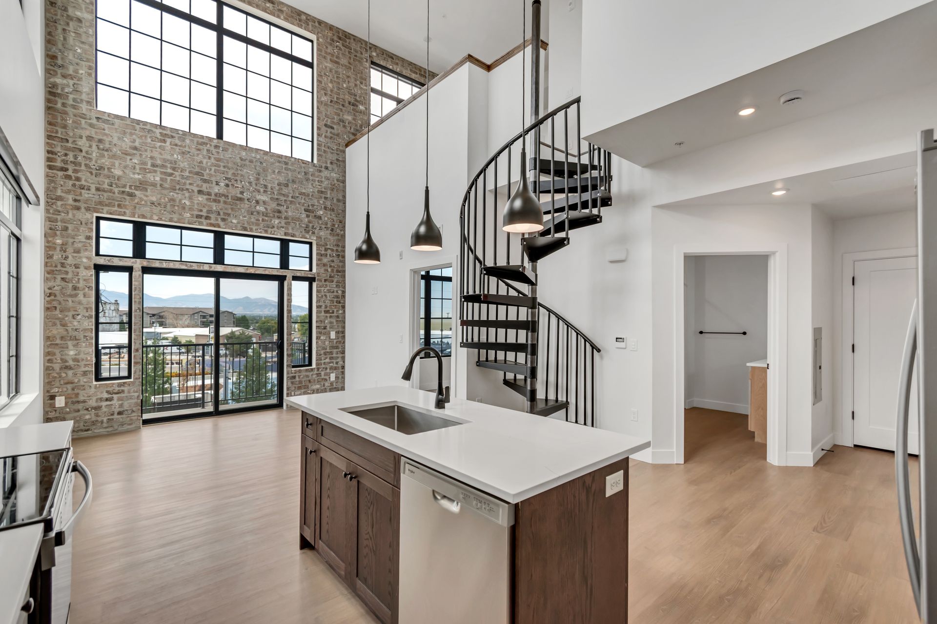 Modern apartment interior with a spiral staircase, exposed brick wall, and a kitchen island.