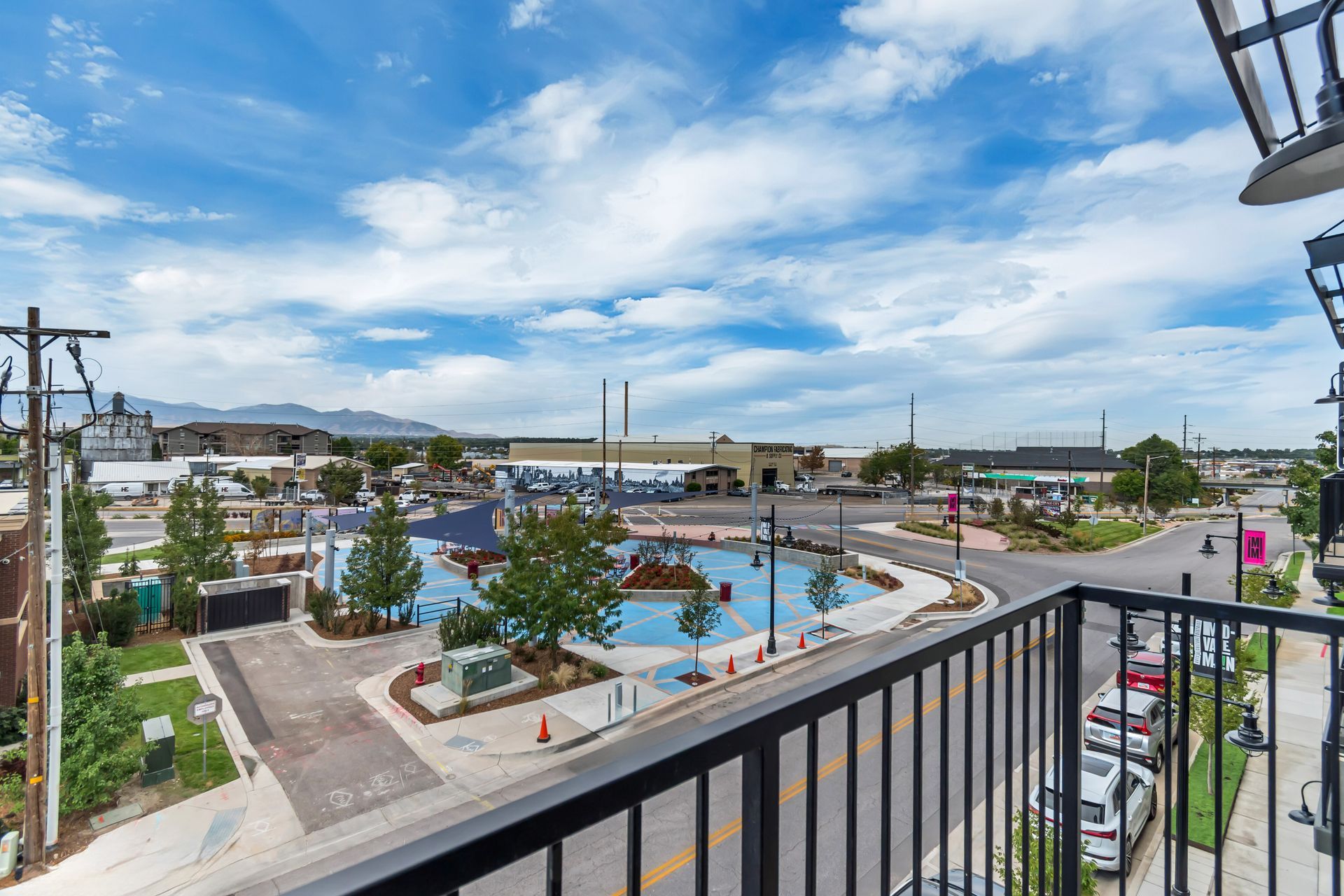 View from a balcony overlooking a park with water features, trees, and buildings on a sunny day.