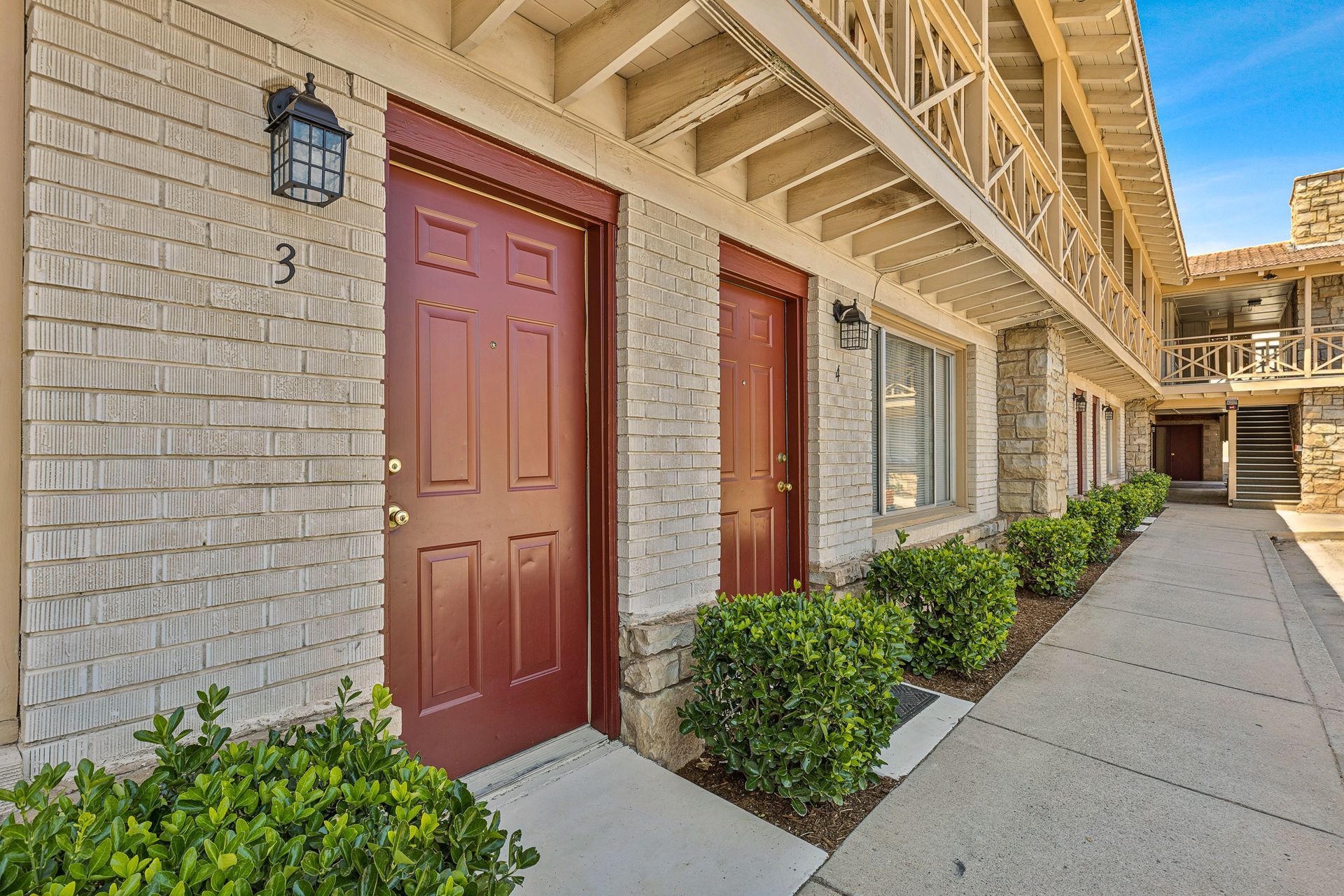 A brick apartment building with red doors and a walkway leading to them.