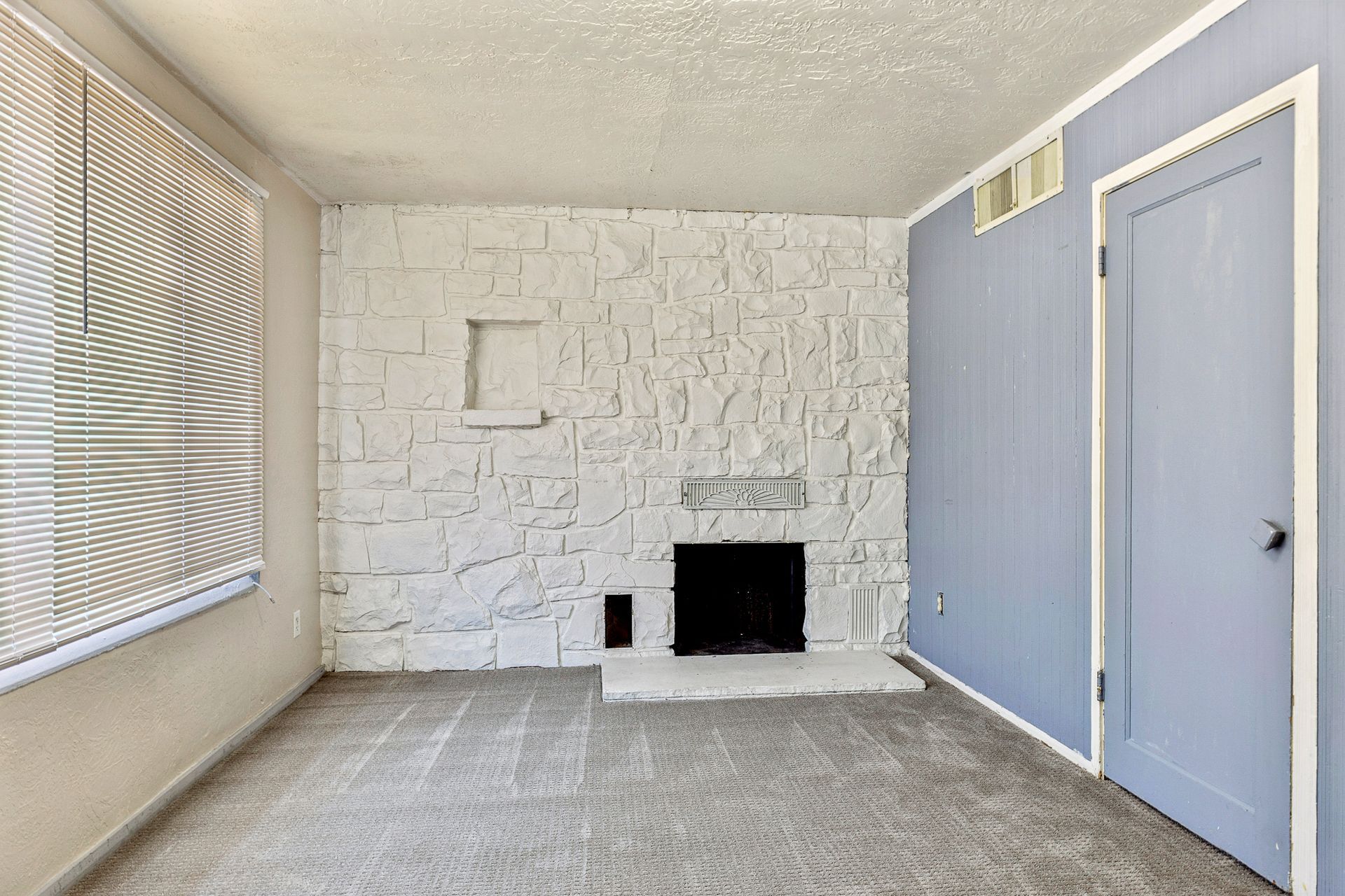 An empty living room with a fireplace and a blue door.