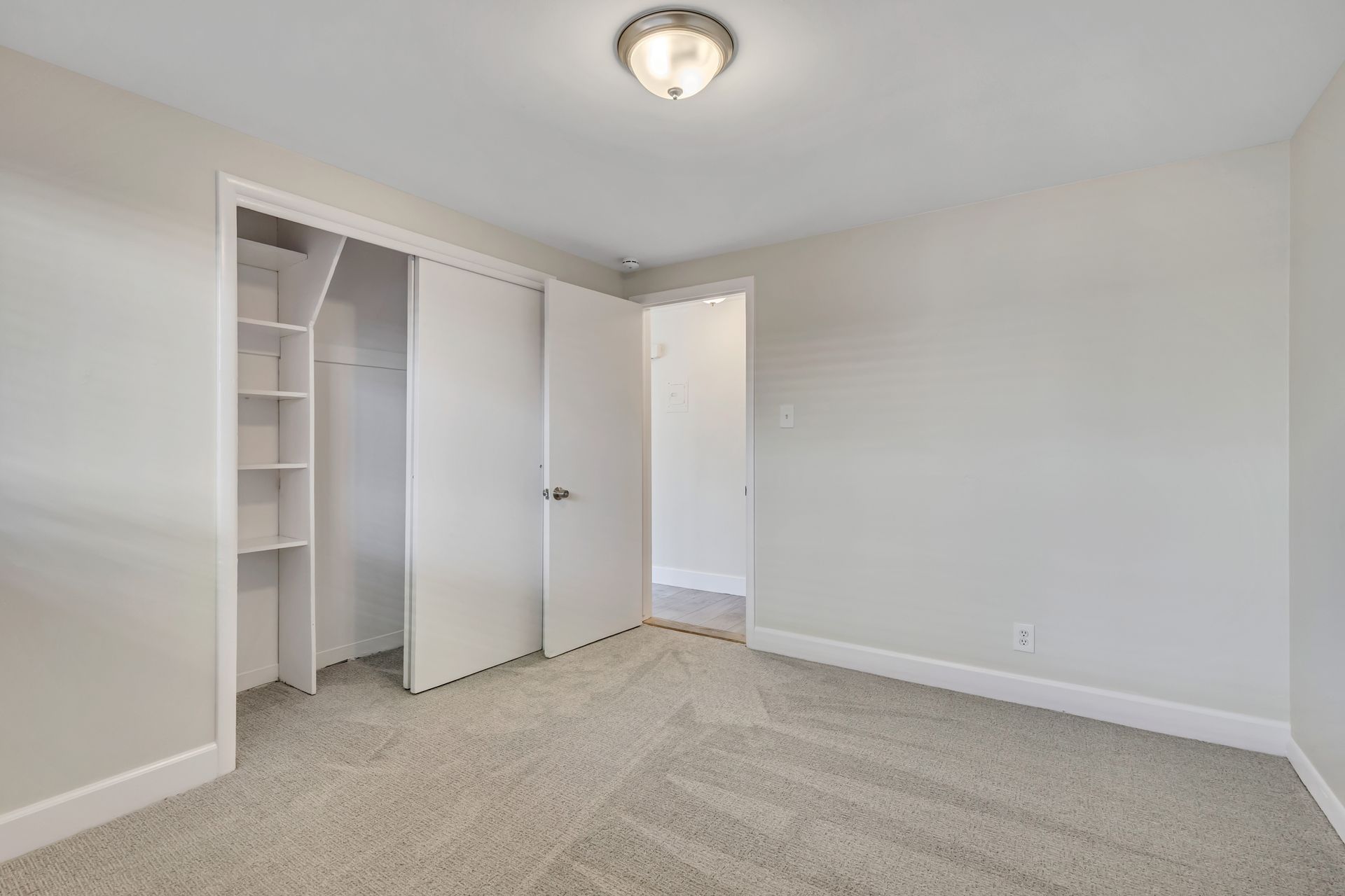 Empty bedroom with closet and doorway; light gray walls, carpet, and white trim.