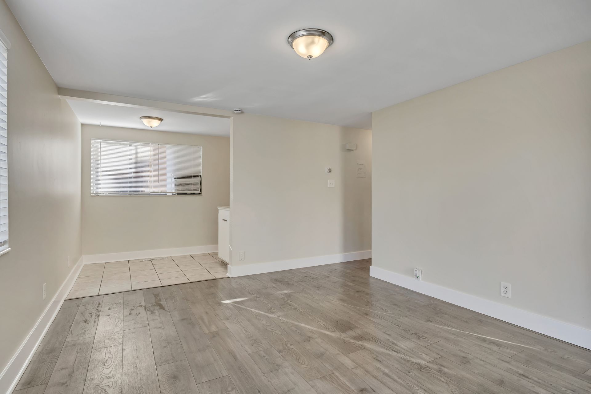 Empty room with wood-look floors, light walls, and a hallway leading to a window.