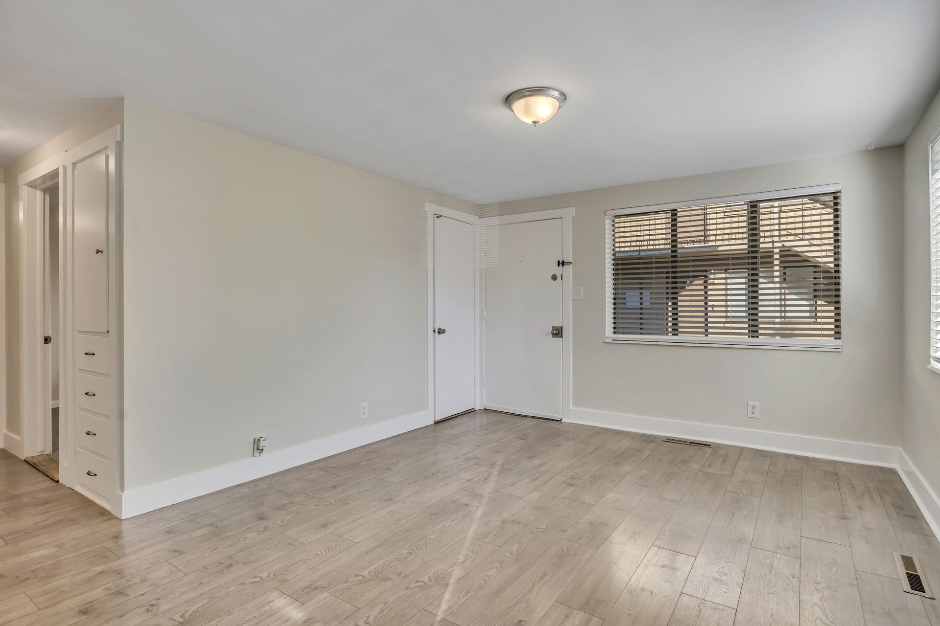 Empty room with light-colored walls, wood floor, and a window with blinds. Includes a closet and closed door.