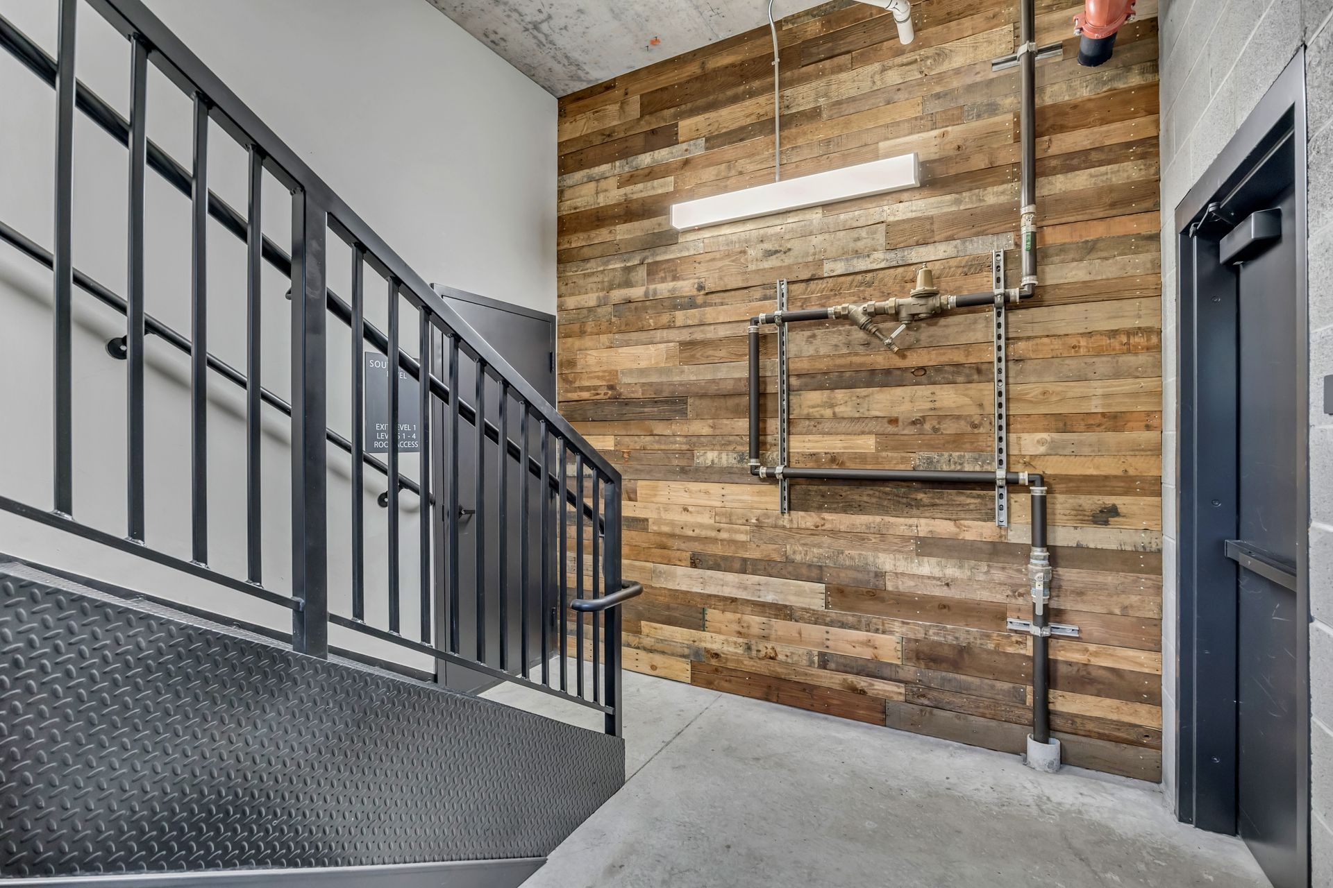 Stairwell with metal staircase, wood-paneled wall, exposed pipes, and elevator.