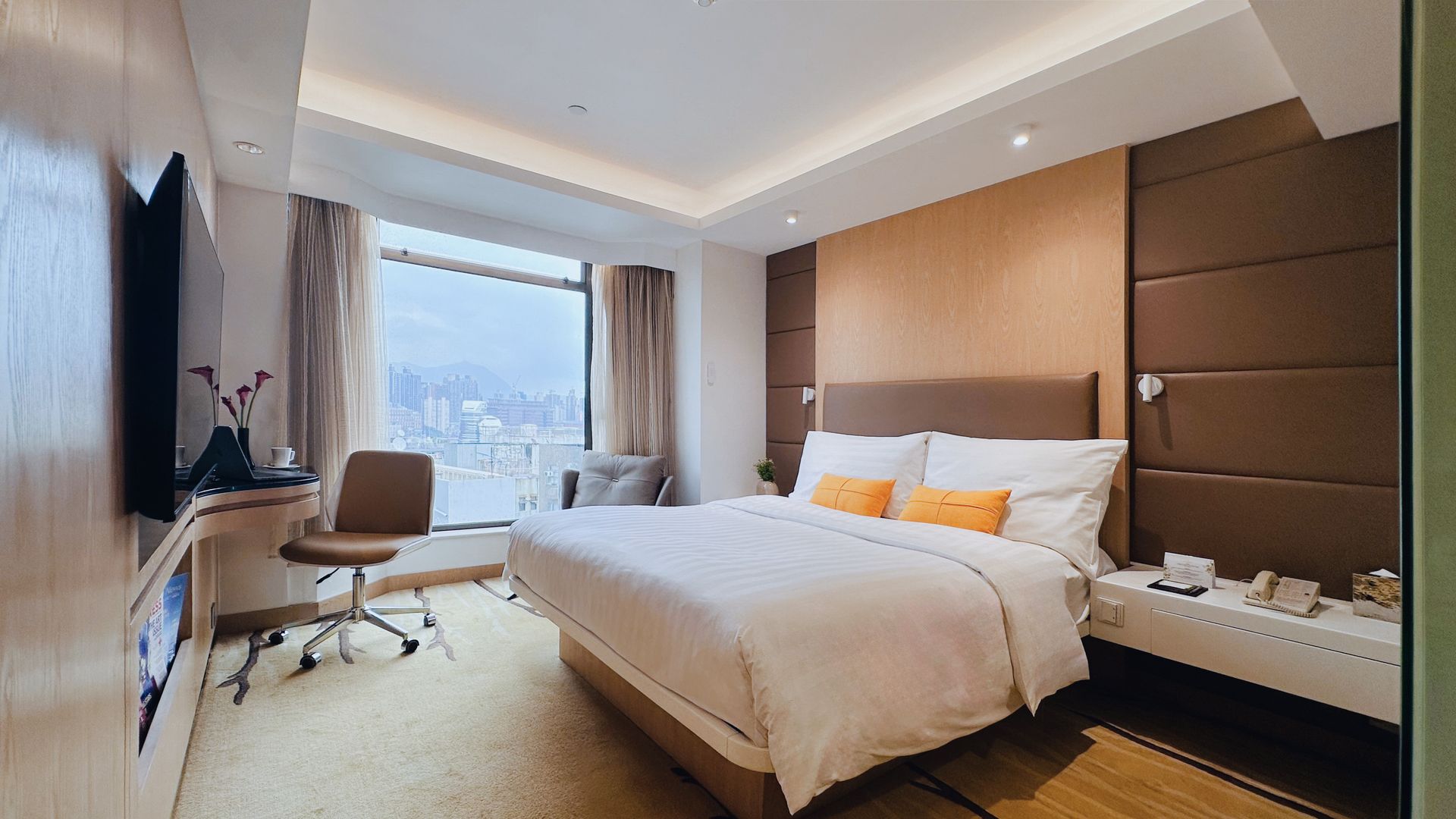 Hotel bedroom with a bed, desk, window, and television. Warm colors and contemporary design.