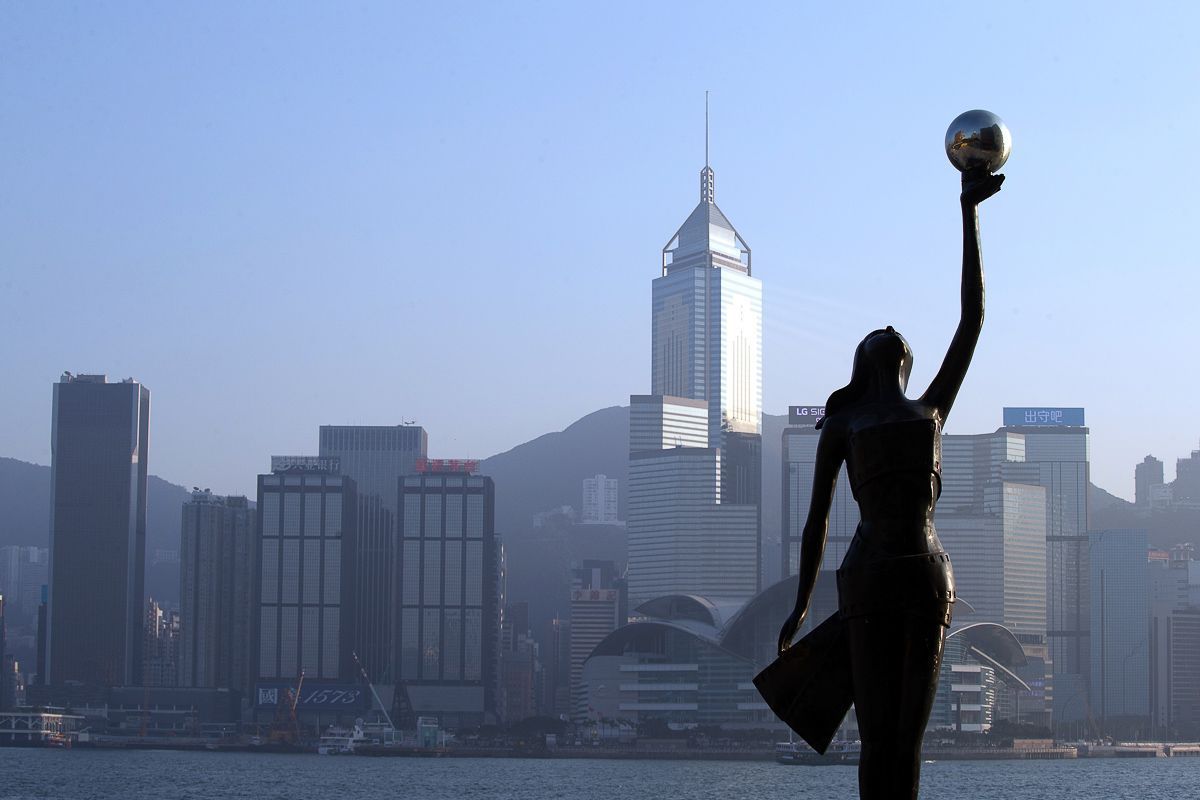 Statue of woman holding a globe, silhouetted against Hong Kong skyline.