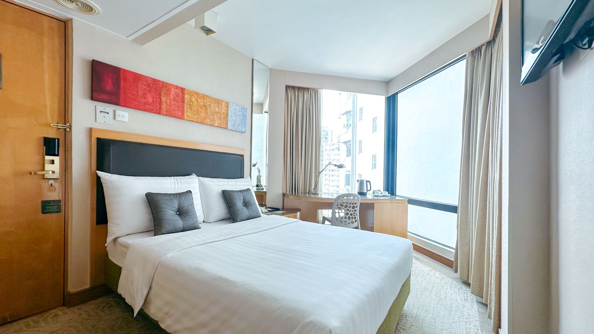 Hotel room with bed, desk with laptop, window with curtains, and art on the wall.