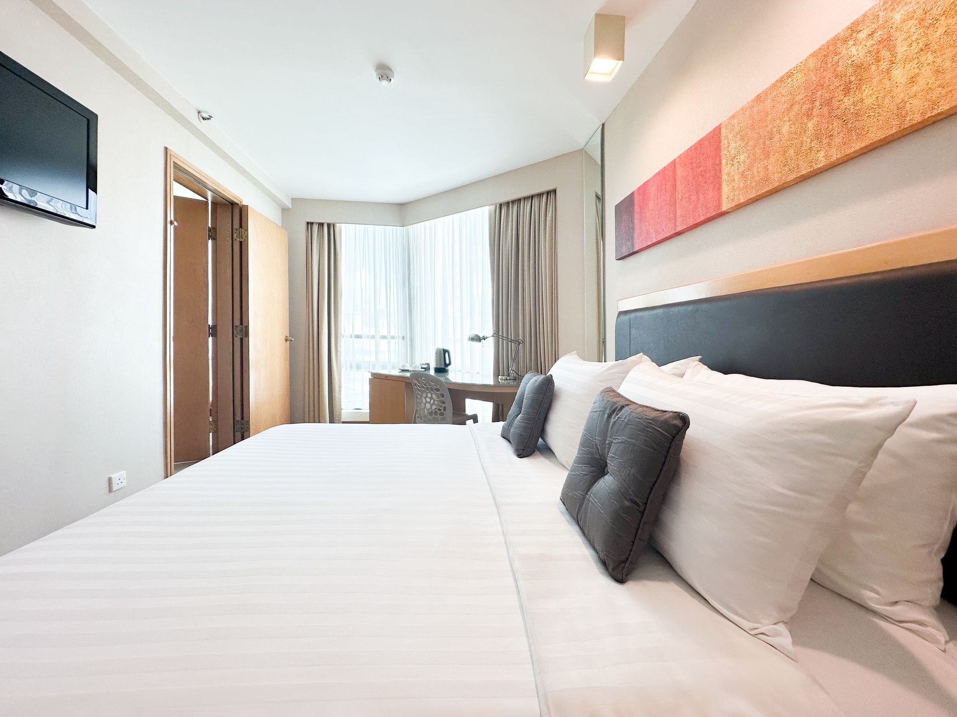 Twin beds in a hotel room with a desk, window, and floral painting.