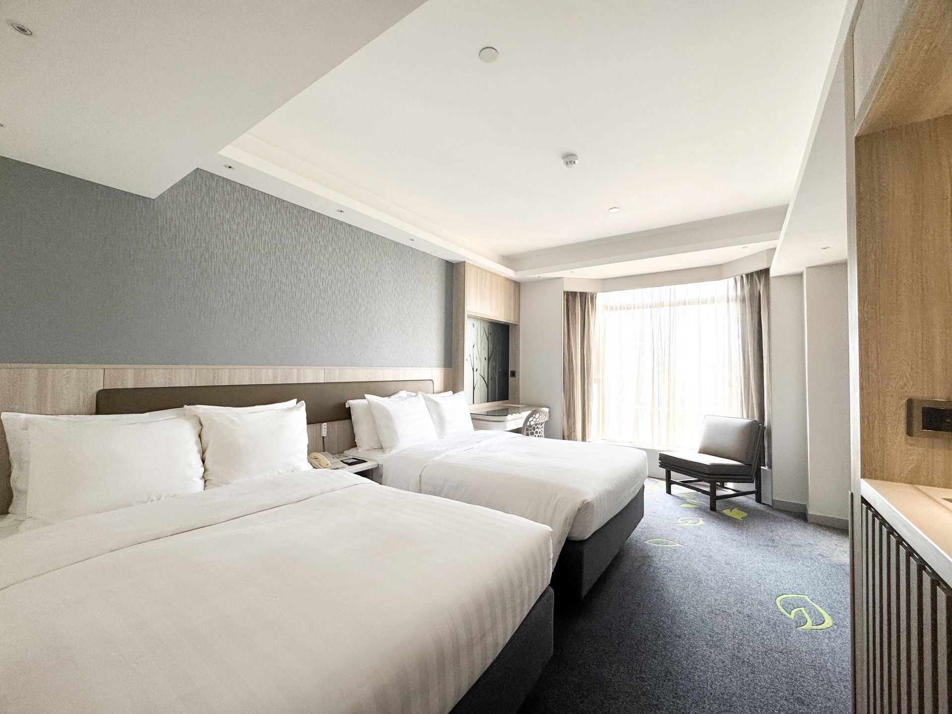 Hotel room with two white beds, gray accent wall, and a bright window with curtains