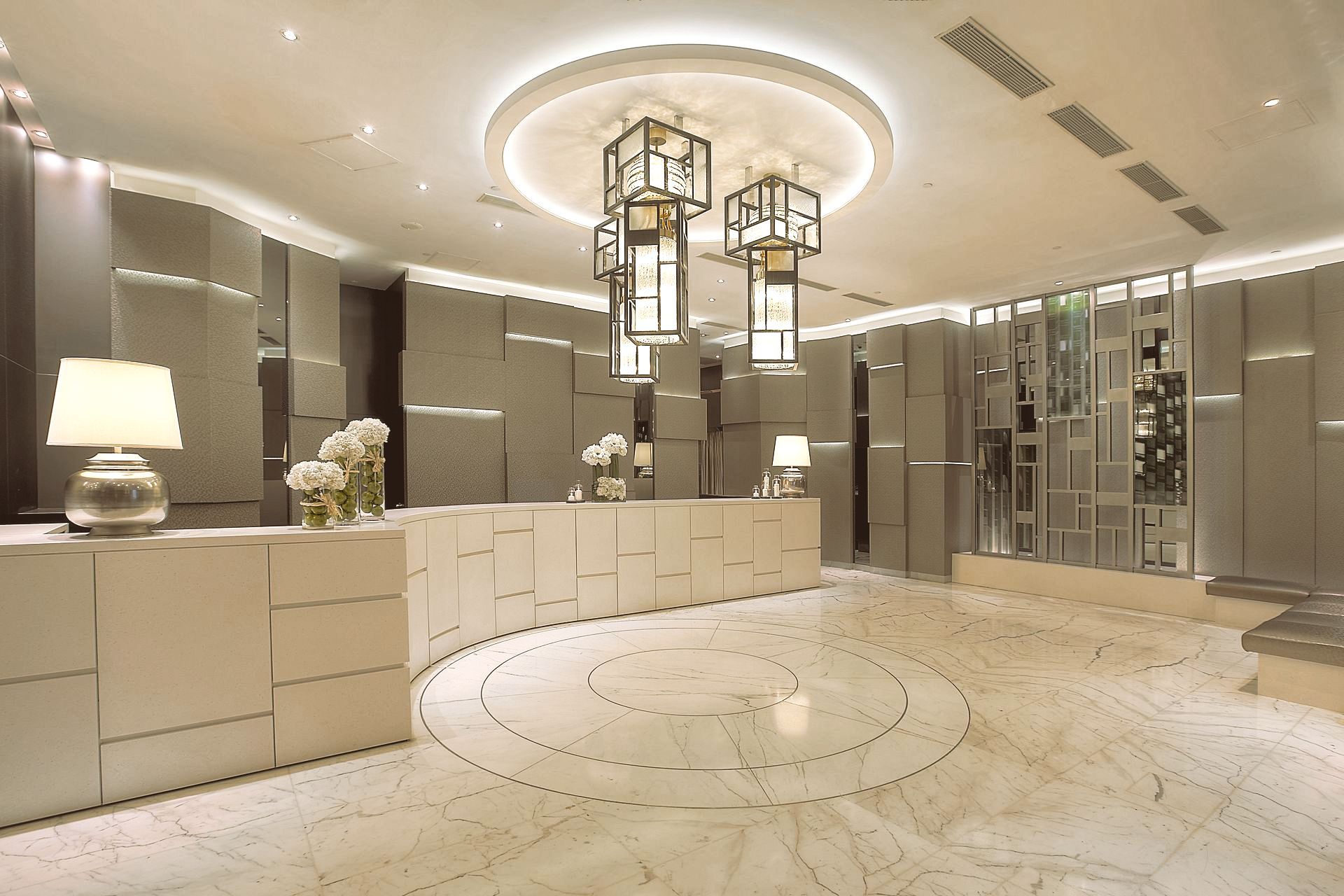 Modern hotel lobby with a curved reception desk, marble floor, and decorative lighting.