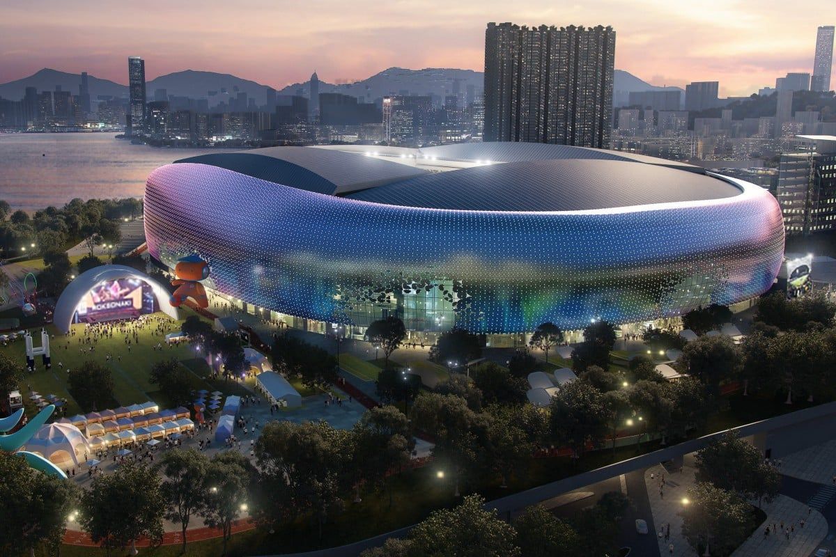 An illuminated, colorful stadium at dusk with a concert in the foreground, city skyline in the distance.