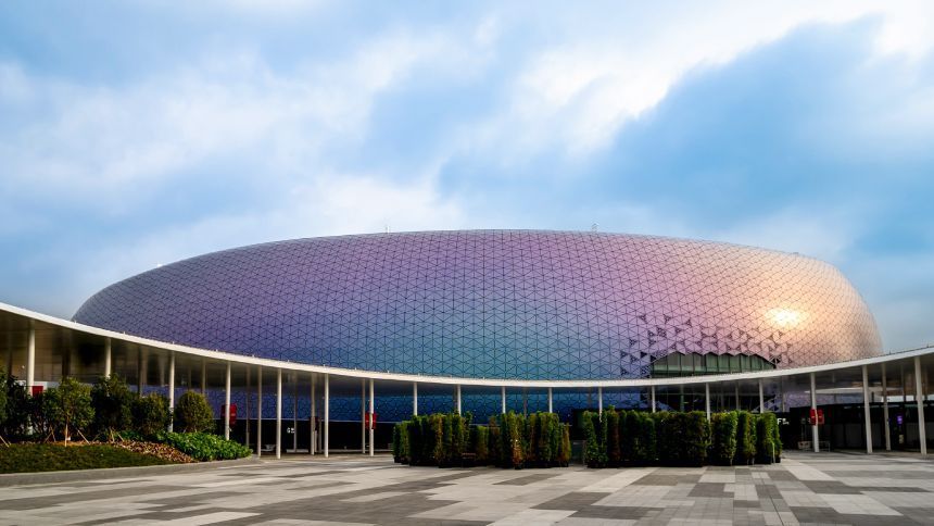 A large, dome-shaped building with colorful, iridescent exterior, next to a curved walkway, against a cloudy sky.