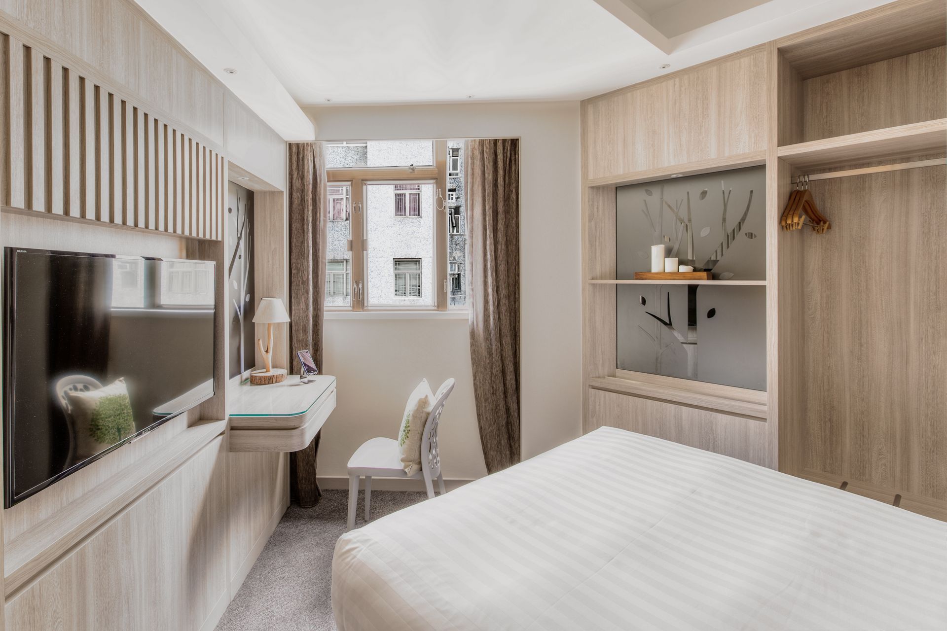 A hotel bedroom with a bed, desk, and television, featuring light wood paneling.