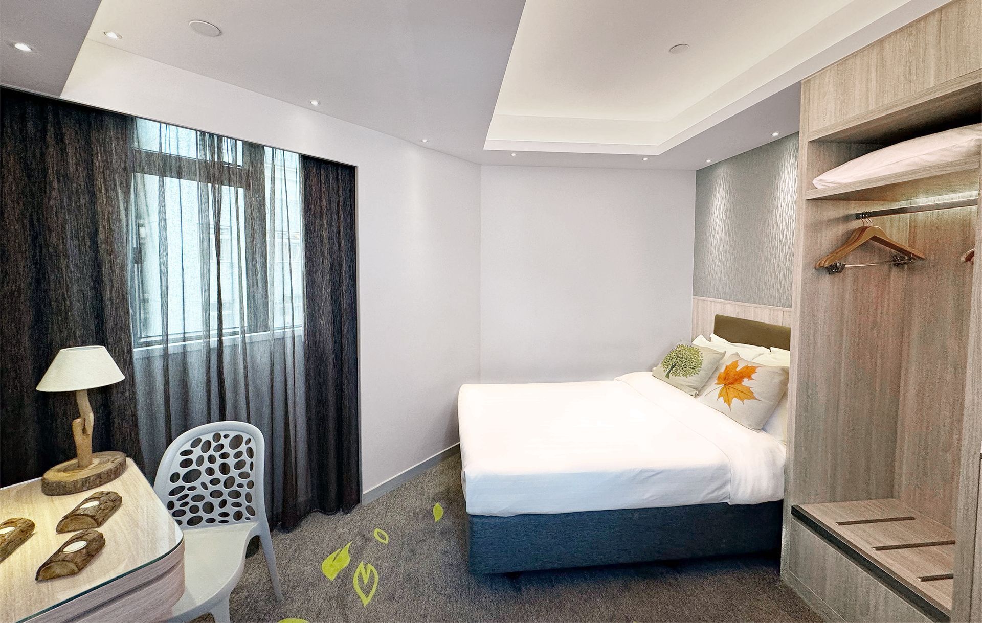 Hotel room with bed, desk, closet, window, gray carpet, and dark curtains.