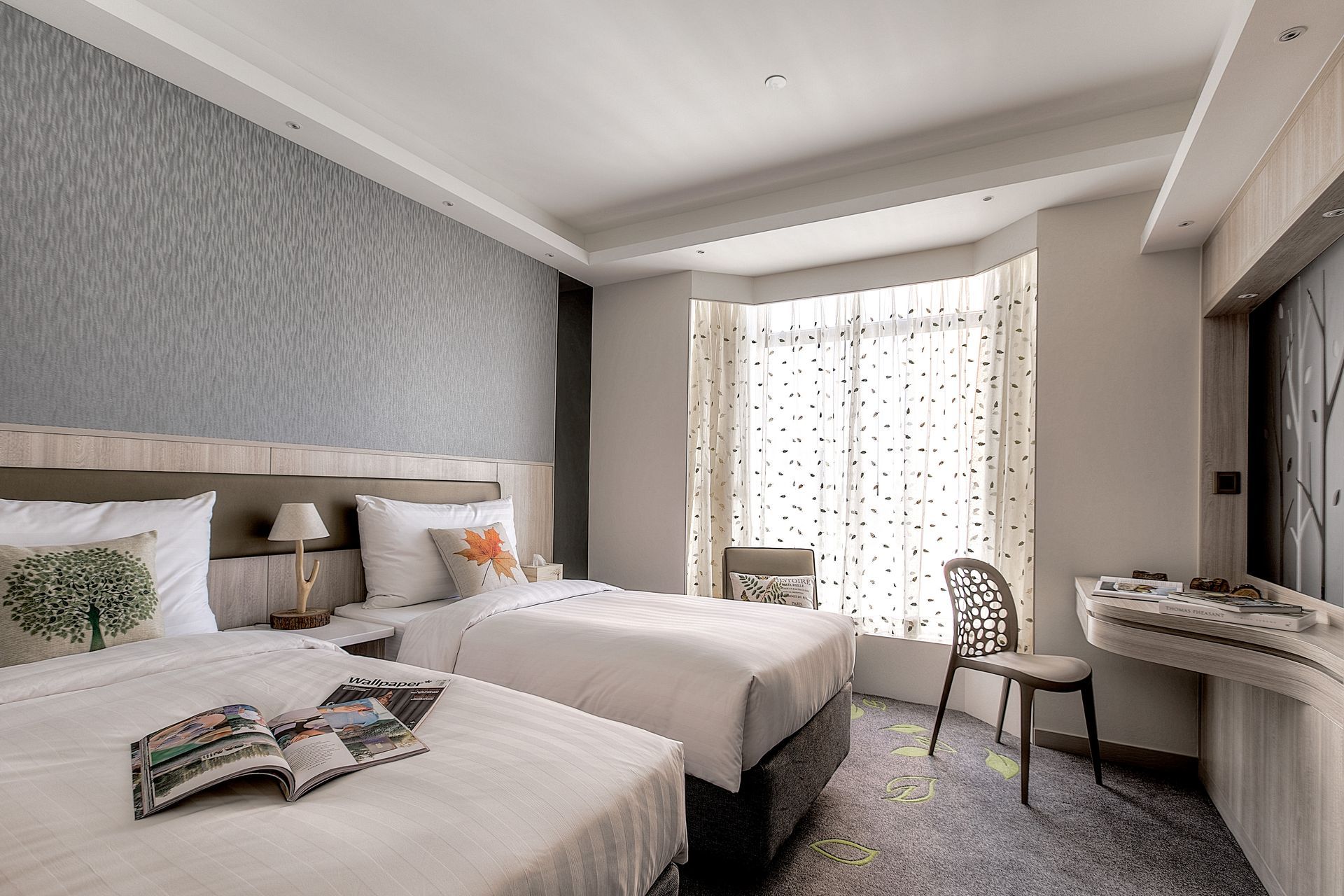 Twin beds in a hotel room with textured gray wall, window, and desk.