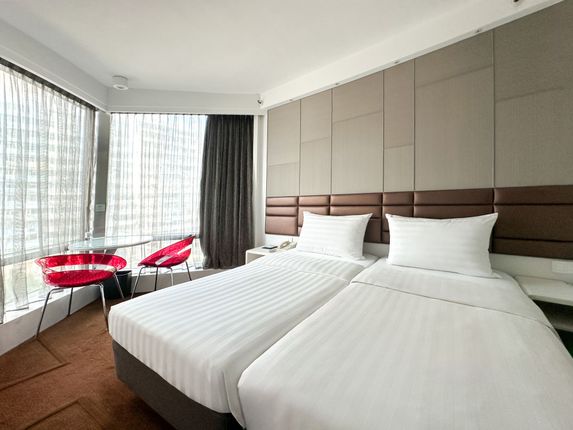 Hotel room with two twin beds, large window, red chairs, and brown accent wall.