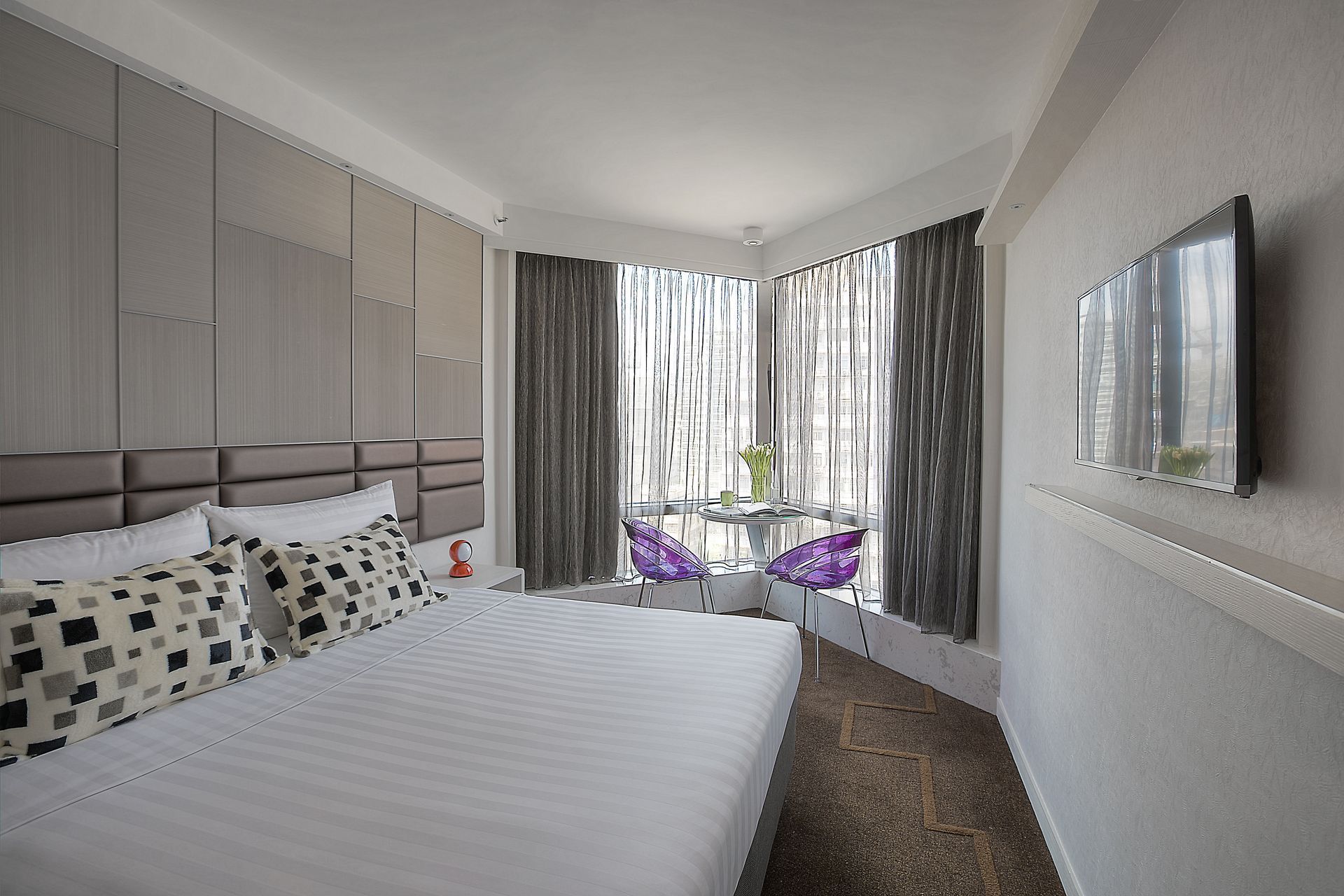 Bedroom with a bed, TV, and a small seating area by a window with curtains.