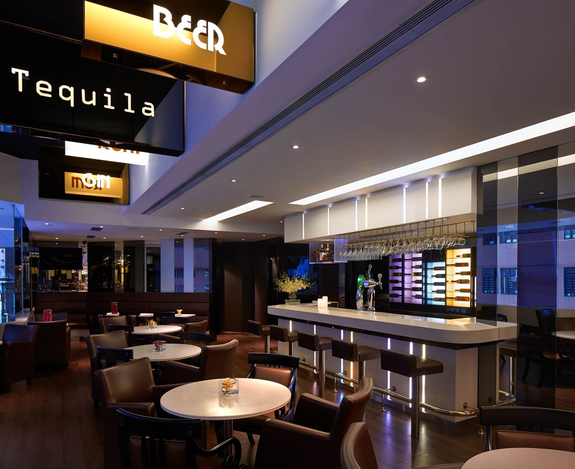 Bar interior with round tables, leather chairs, and a backlit bar with alcohol displays.