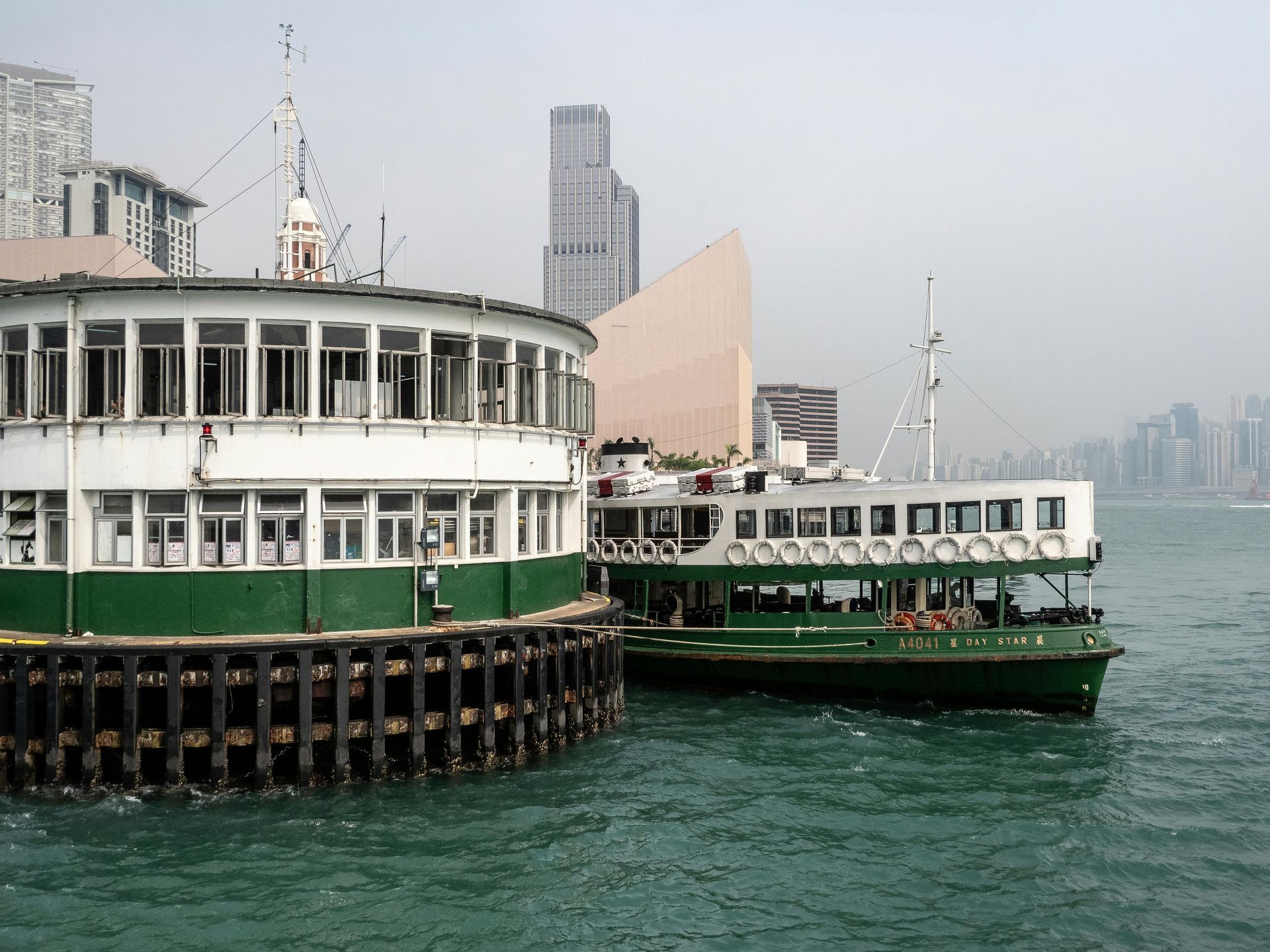 Green and white Star Ferry boats docked at a pier in Hong Kong, with city buildings in the background.