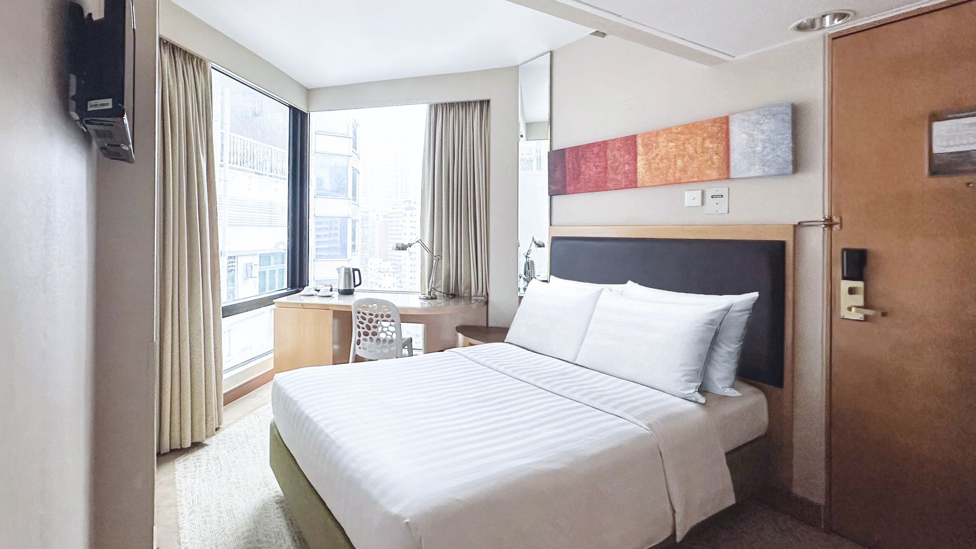 Hotel room with a bed, desk, window, and artwork on the wall.