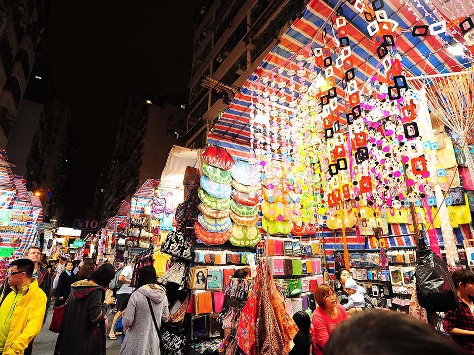 Crowded night market with colorful stalls selling bags, souvenirs, and decorations.