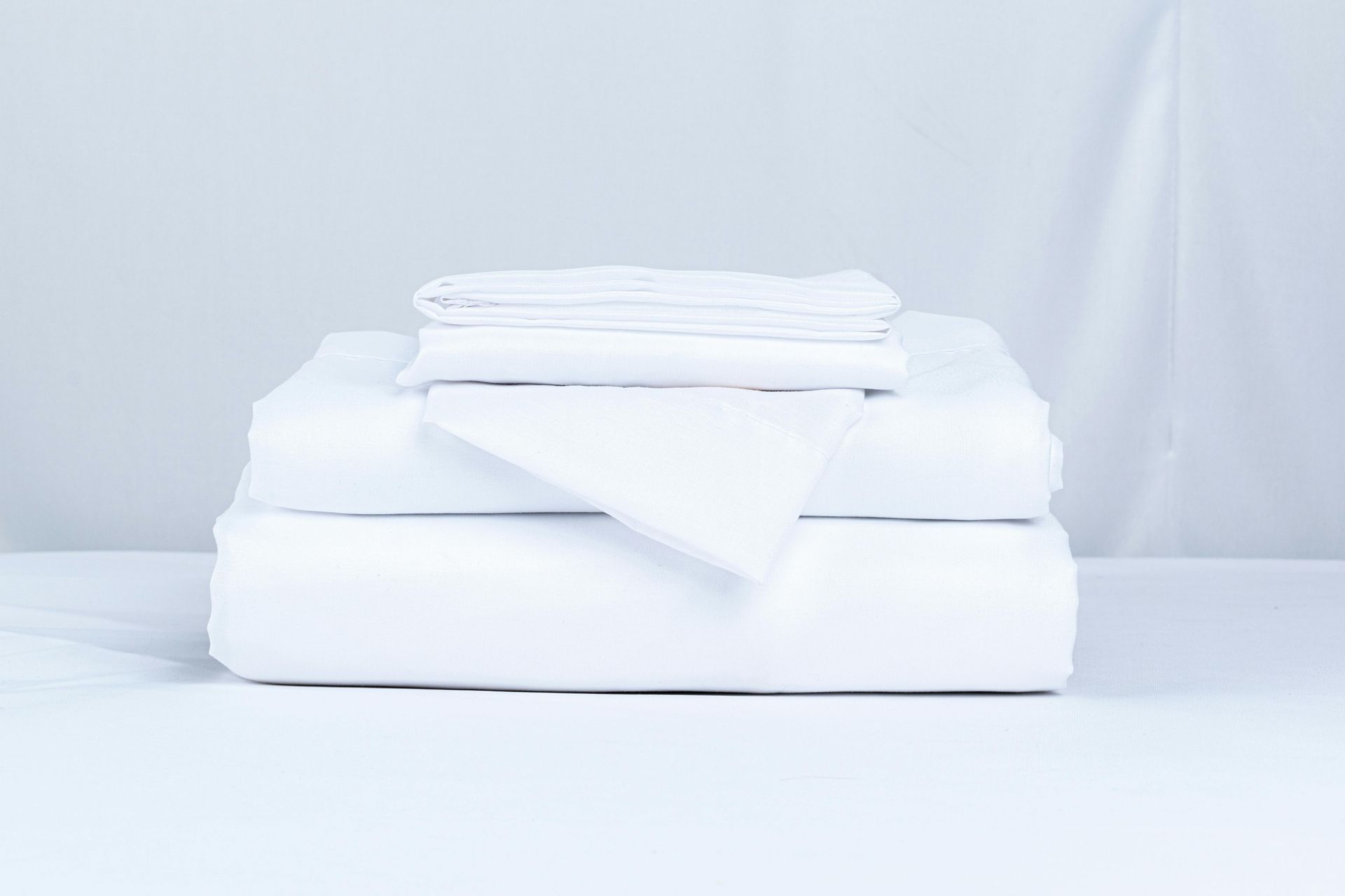 White bed sheet set, folded neatly, with fitted, flat, and pillowcase.