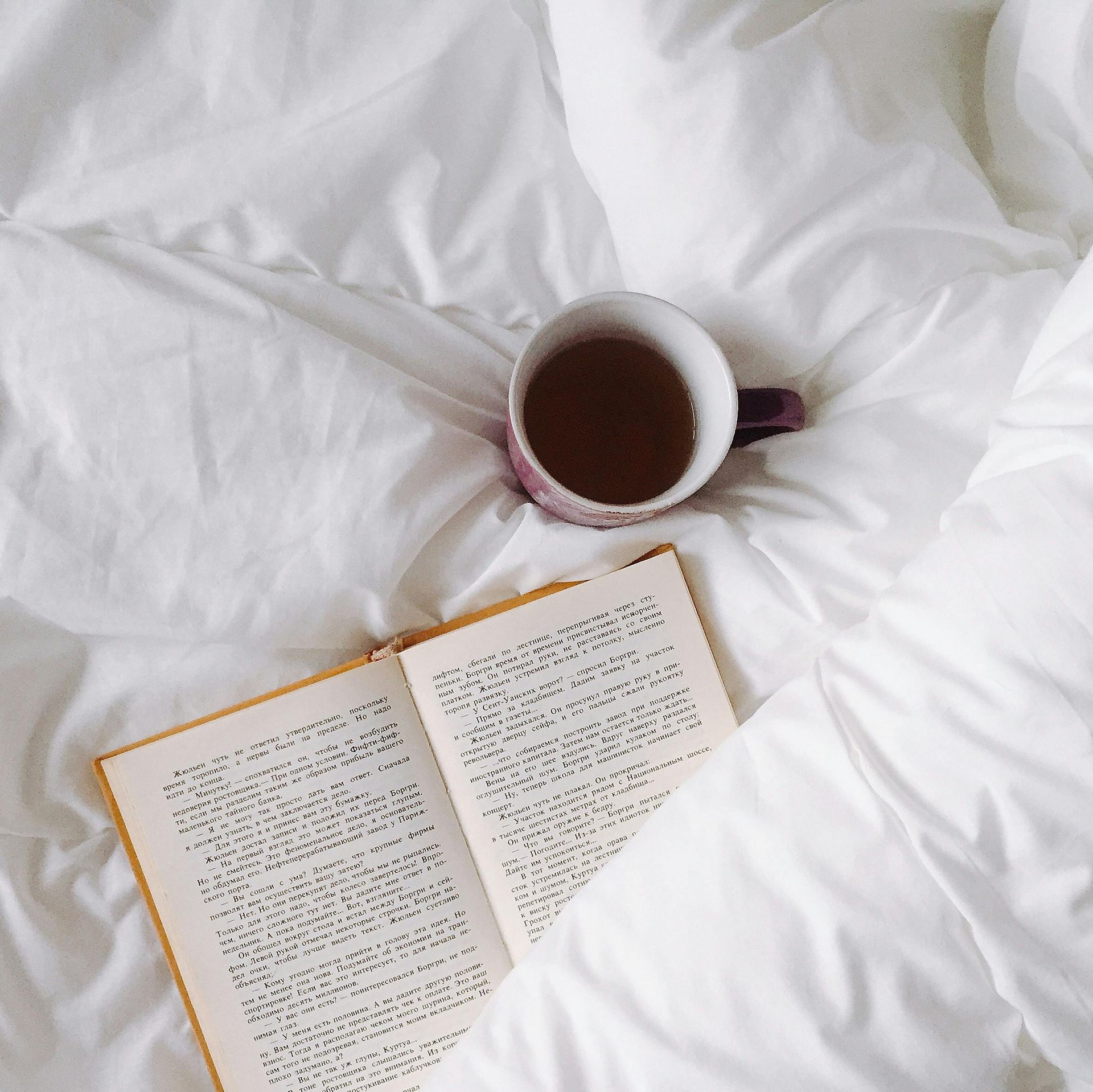 Open book and mug of tea on white bedding.
