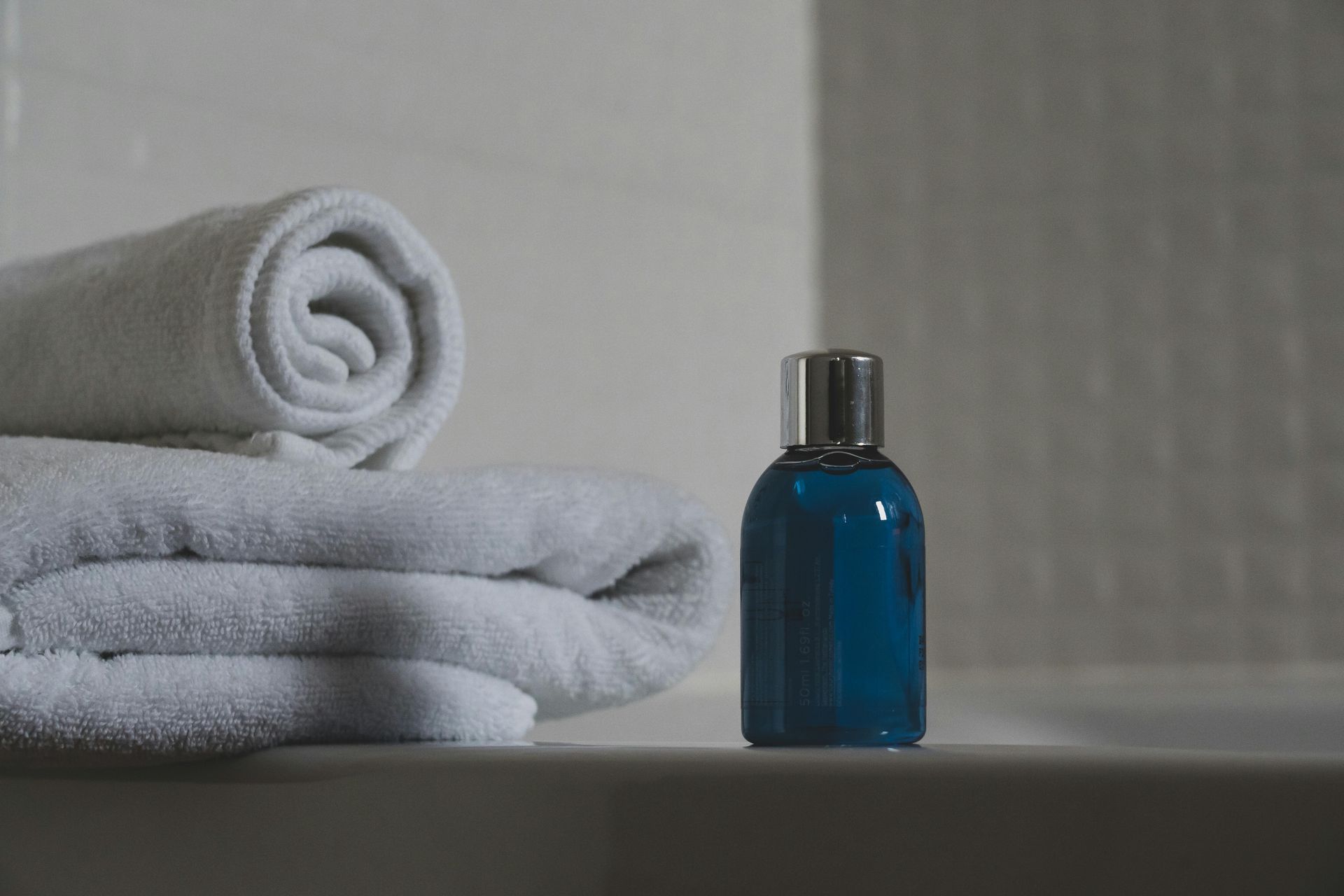 White towels stacked and rolled, with a blue bottle of liquid on a white surface.
