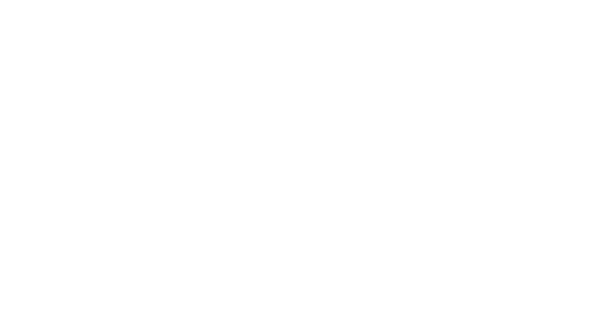 Un homme vêtu d'un blazer beige et d'une chemise blanche se tient debout dans un studio baigné de lumière, gesticulant tout en parlant.