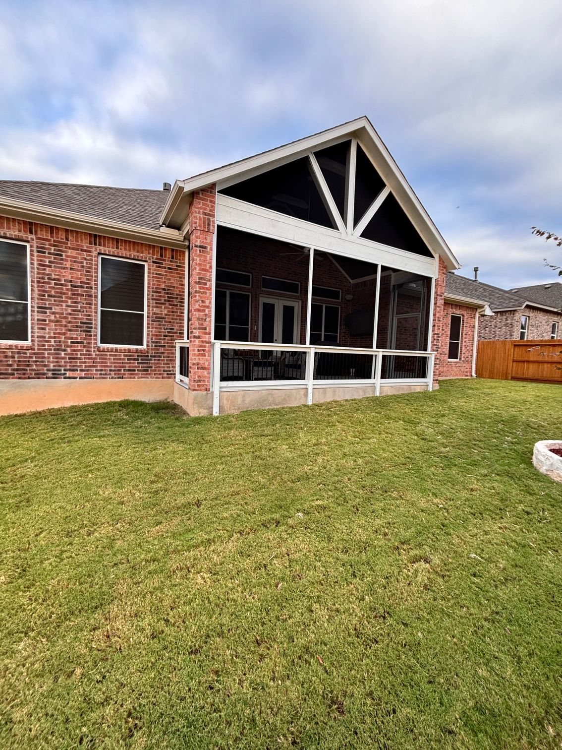 A brick house with a screened in porch and a large lawn in front of it.
