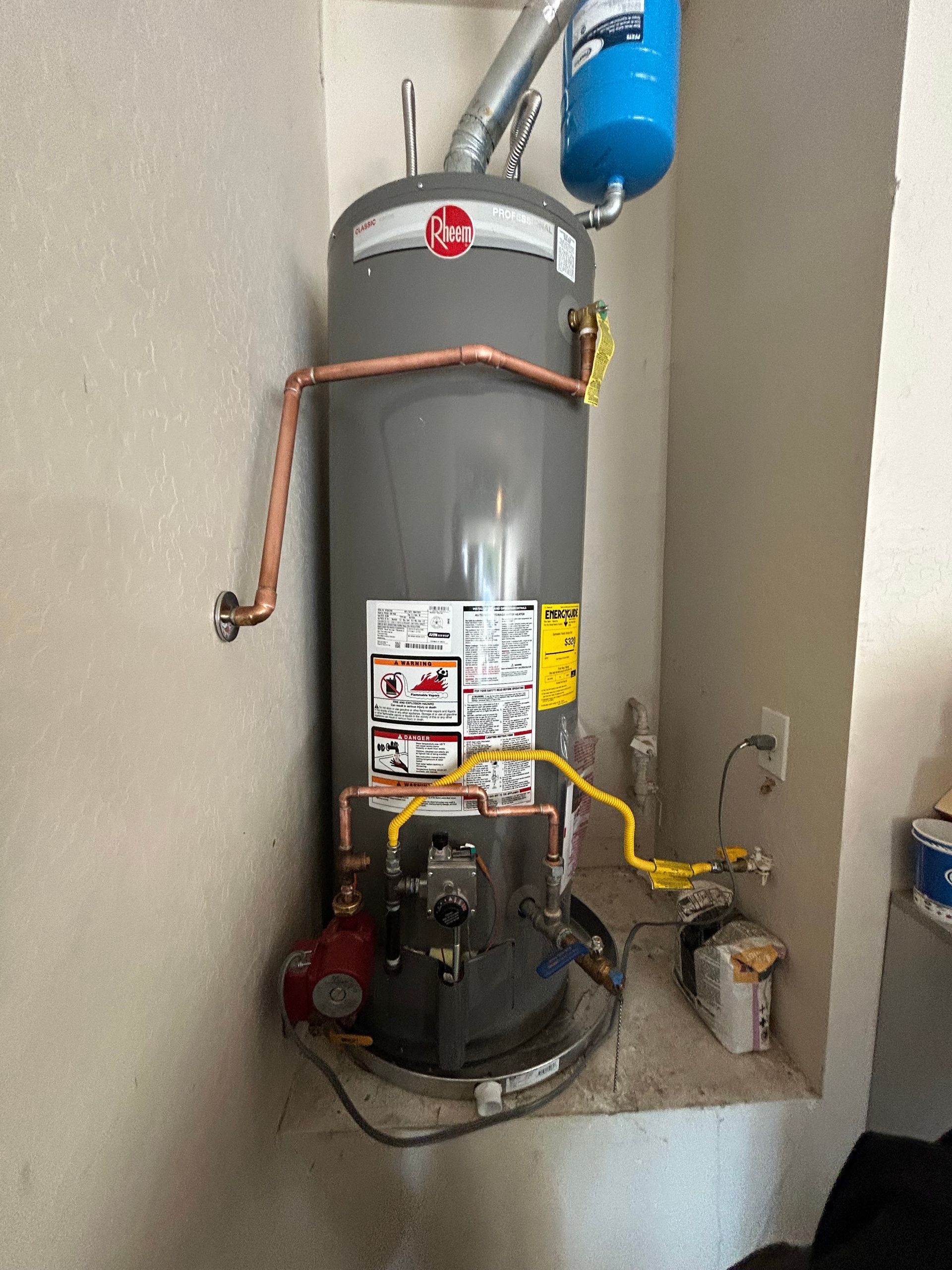 A water heater is sitting in a corner of a room next to a wall.