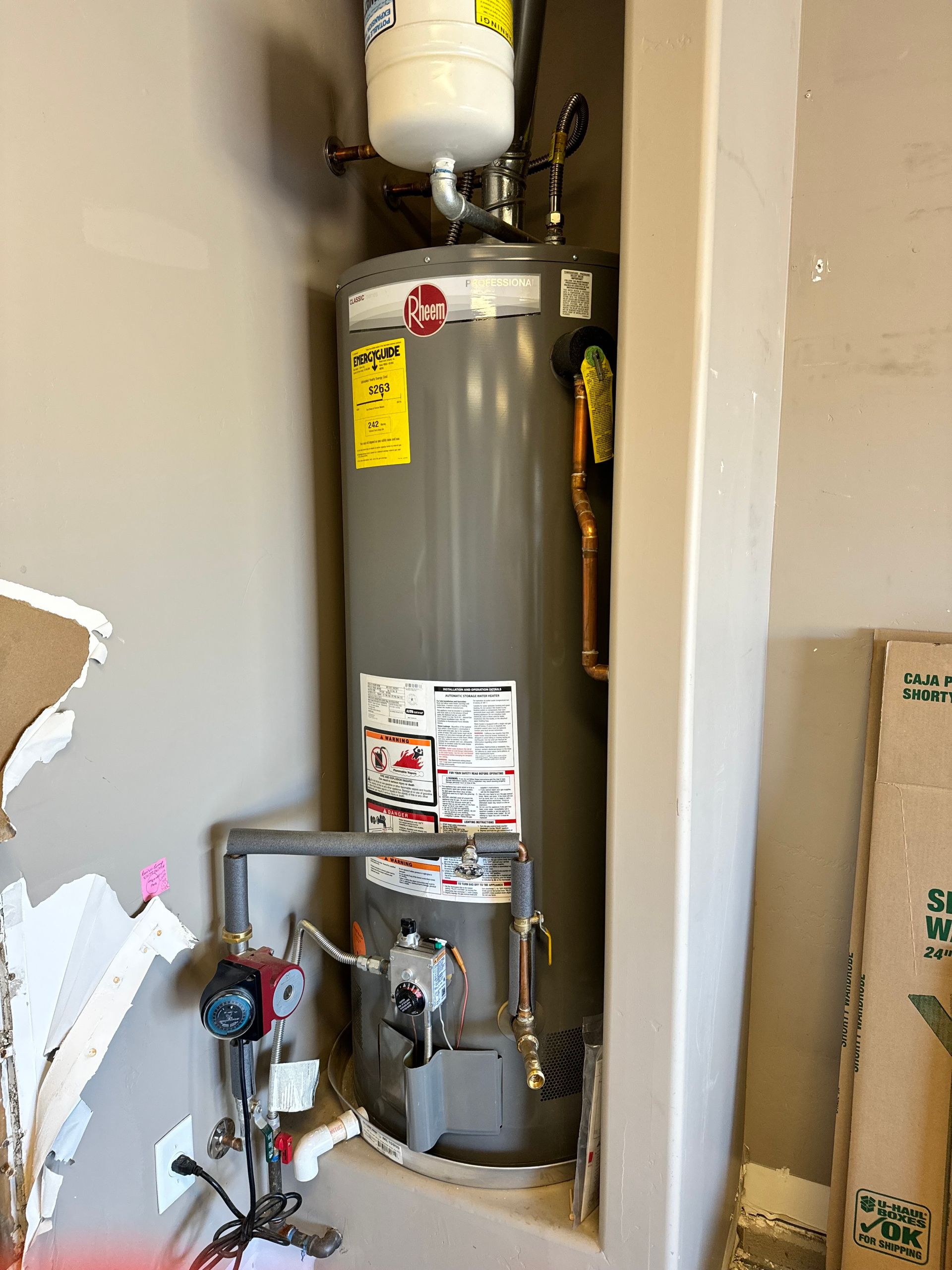 A water heater is sitting in a corner of a room.