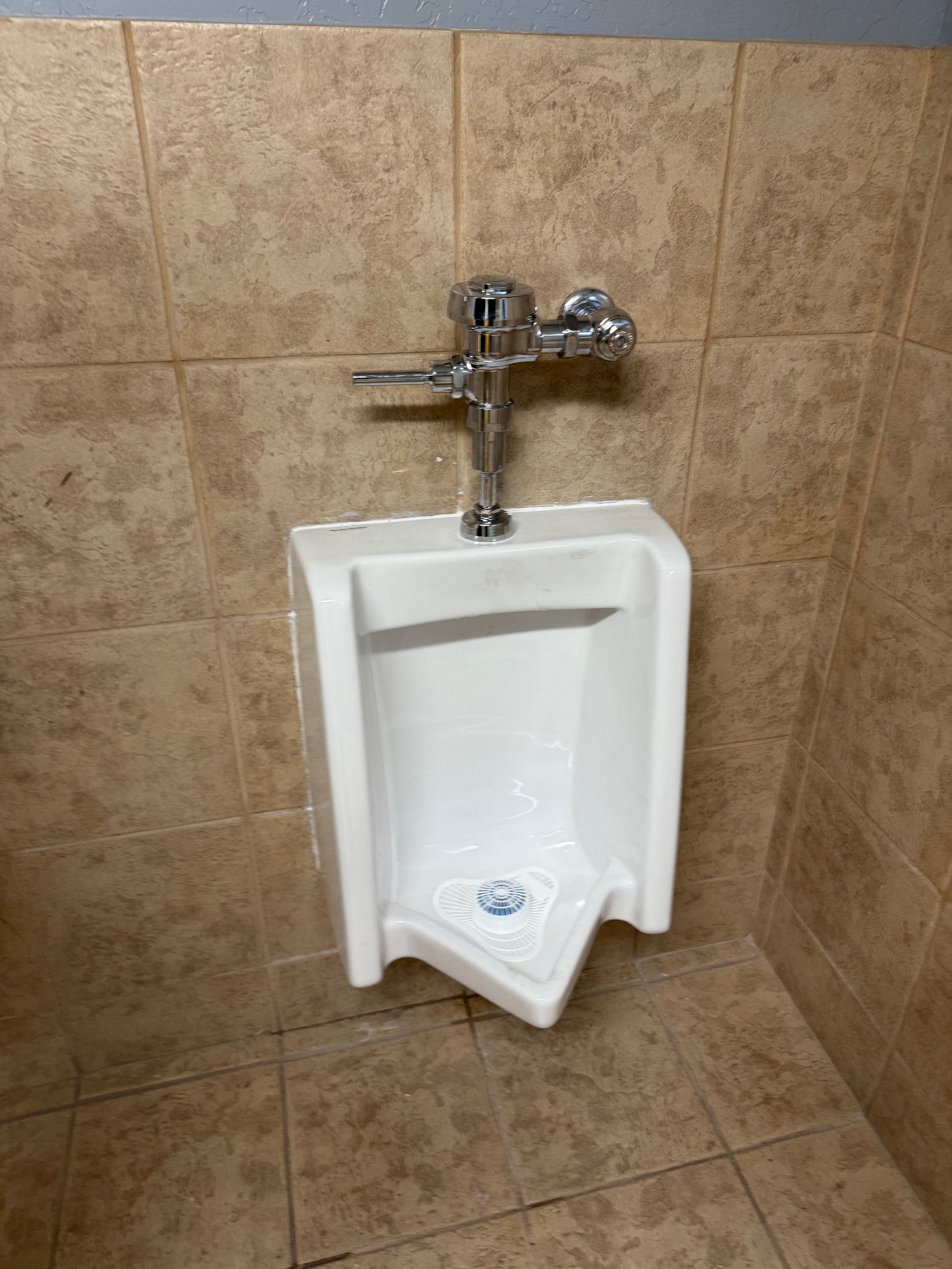A white urinal is sitting in a bathroom next to a tiled wall.