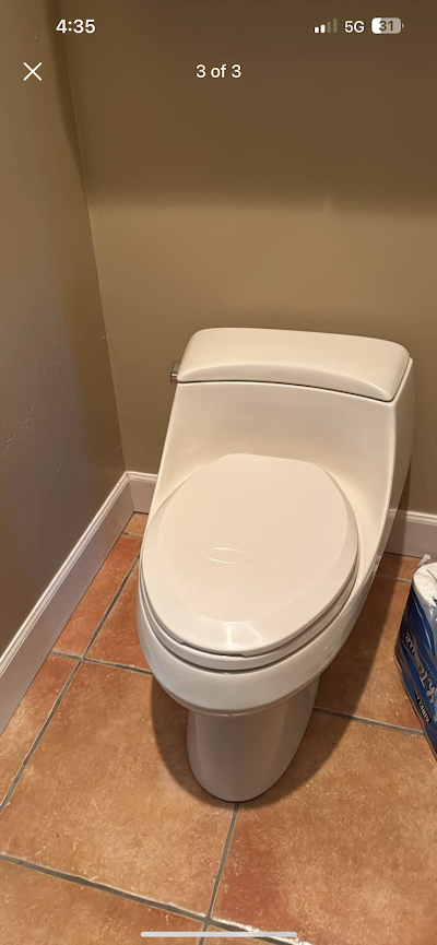 A white toilet is sitting on a tiled floor in a bathroom.