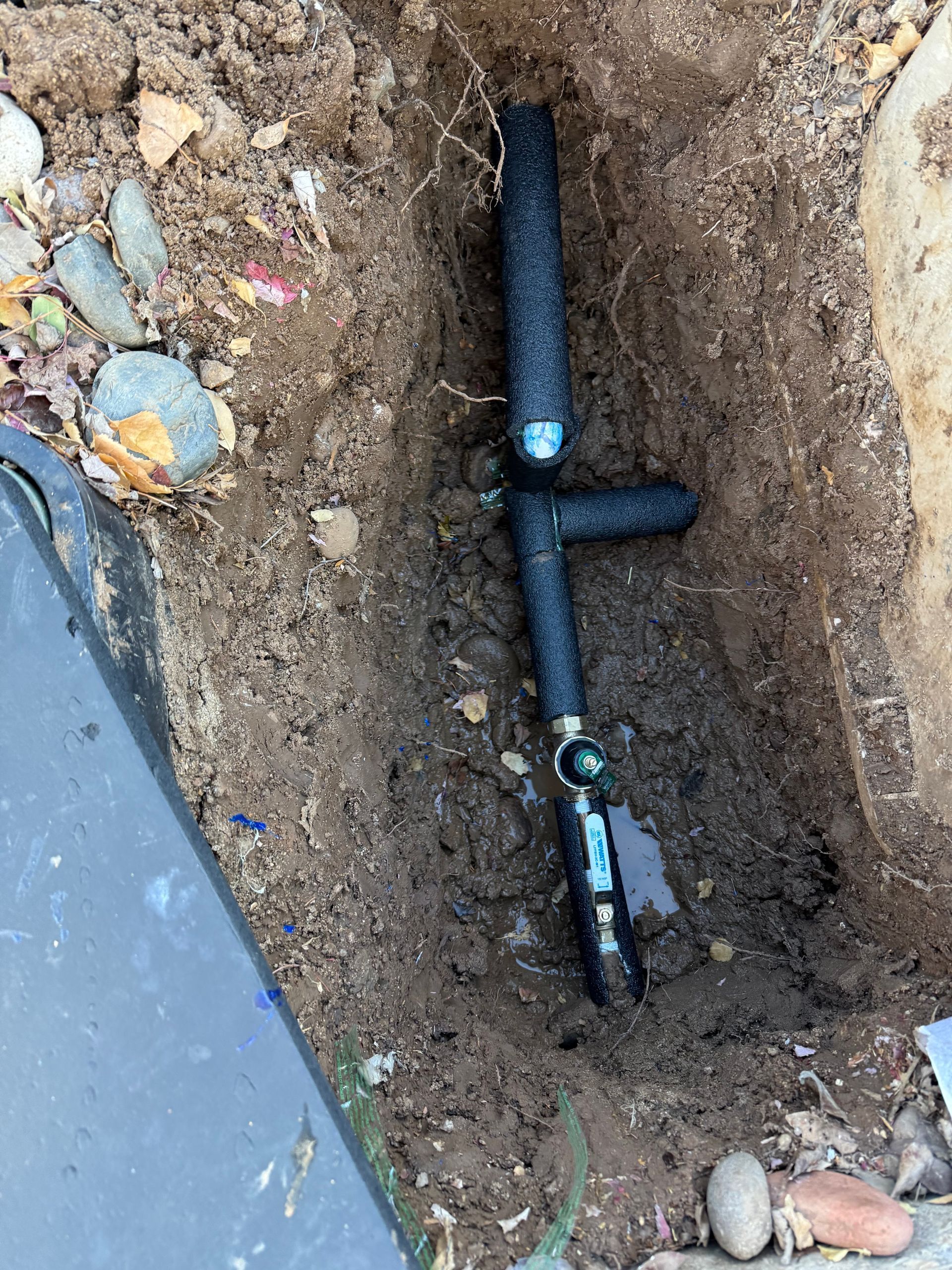 A black pipe is laying in the dirt in a hole.