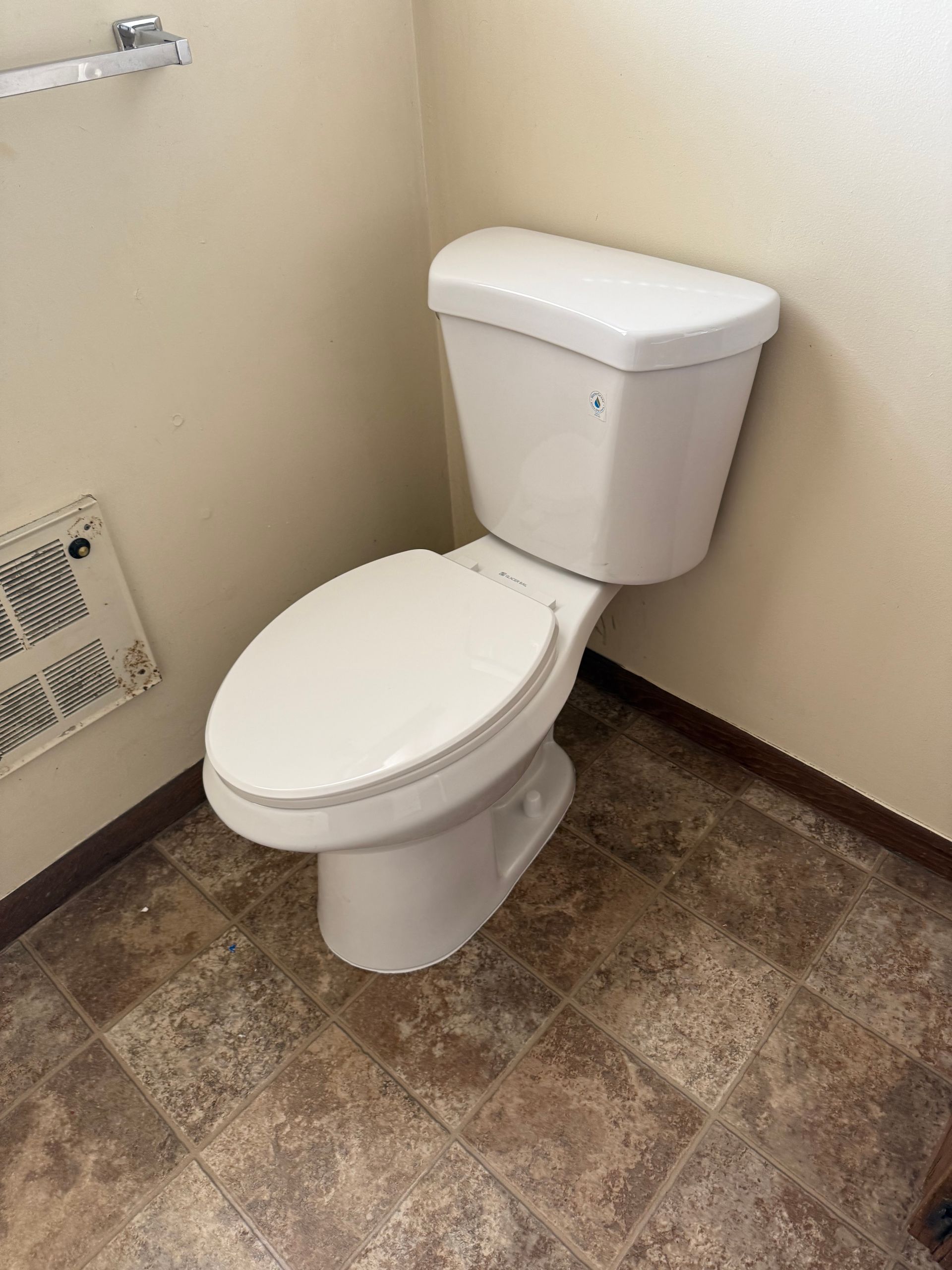 A white toilet is sitting on a tiled floor in a bathroom.