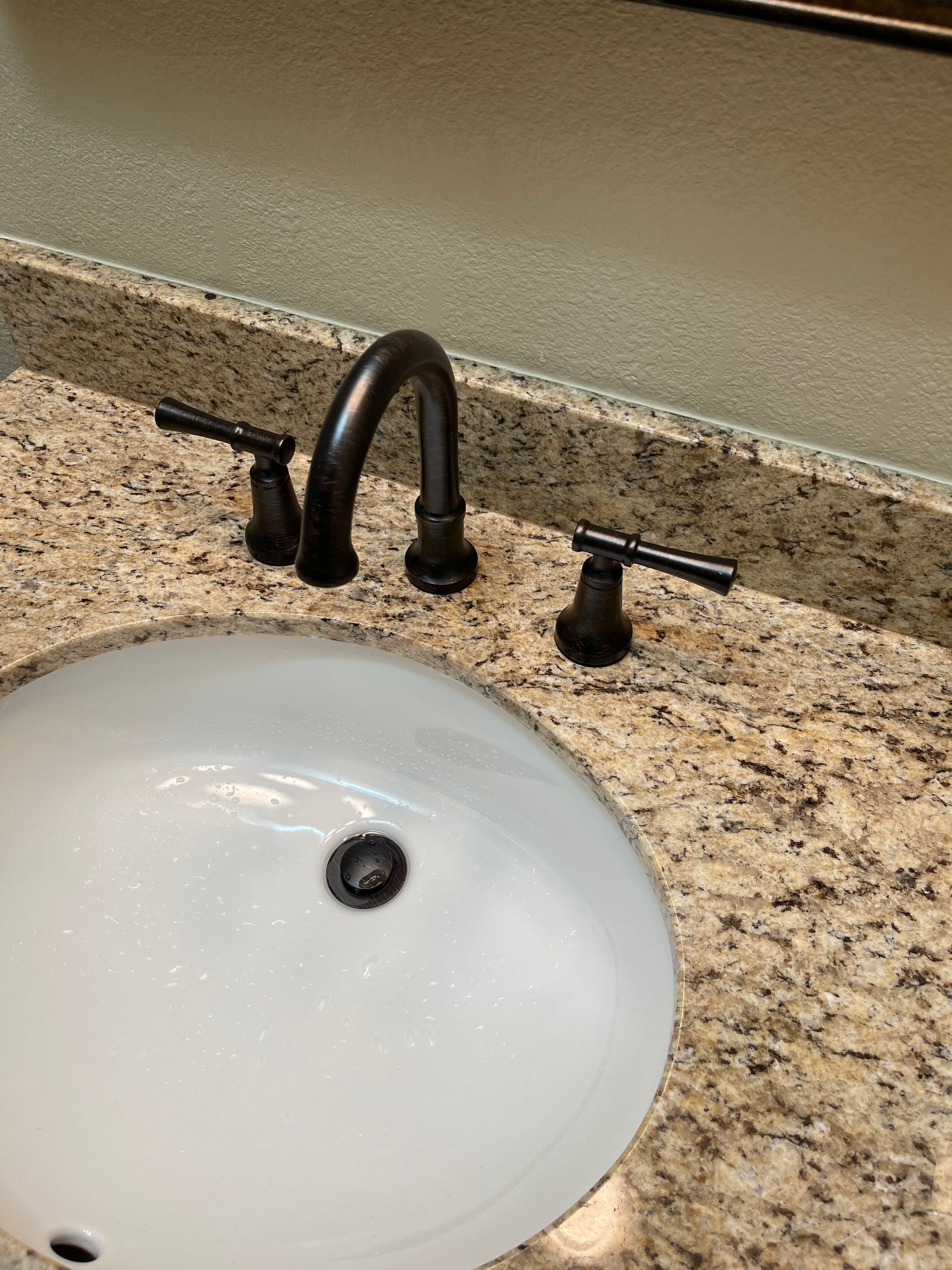 A bathroom sink with a black faucet on a granite counter top.