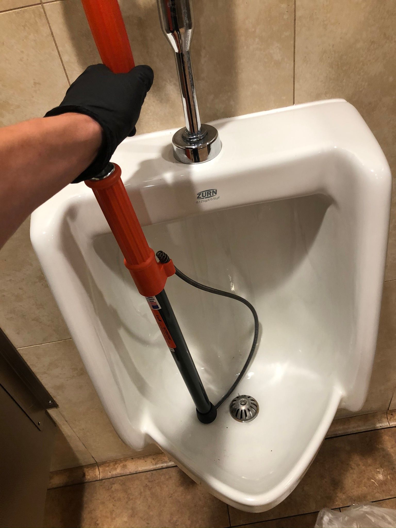 A person is holding a plunger over a urinal.