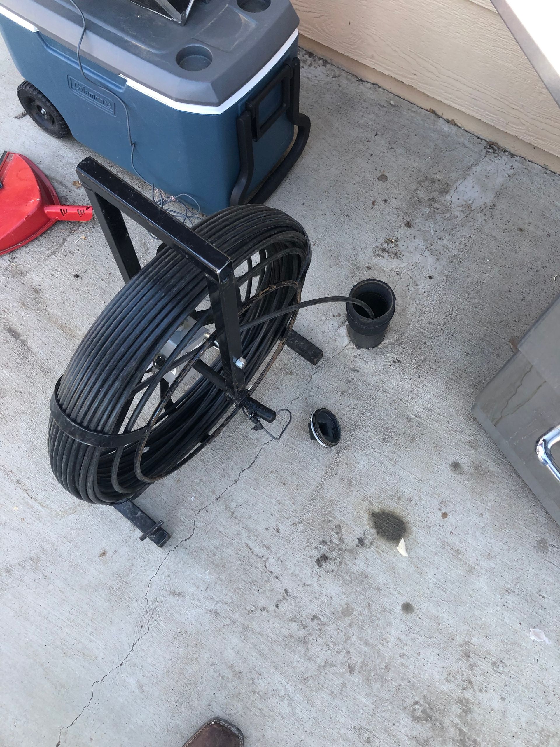 A drain snake is sitting on the ground next to a cooler.