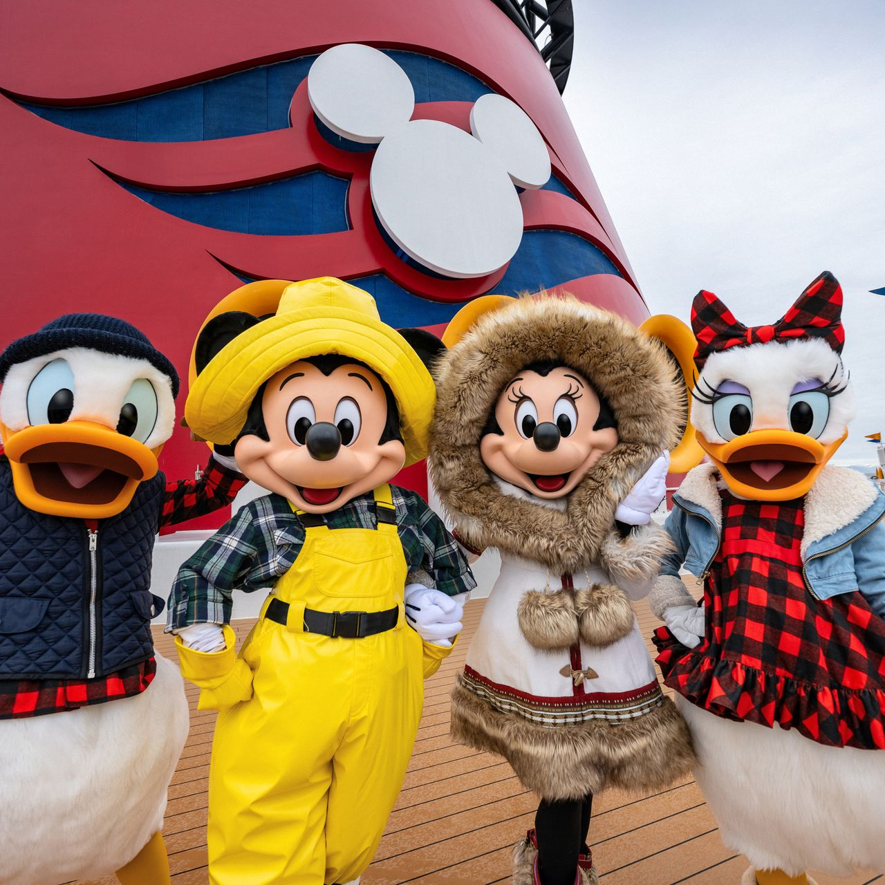 Donald Duck, Mickey Mouse, Minnie Mouse, and Daisy Duck pose in winter outfits in front of a Disney Cruise Line funnel.