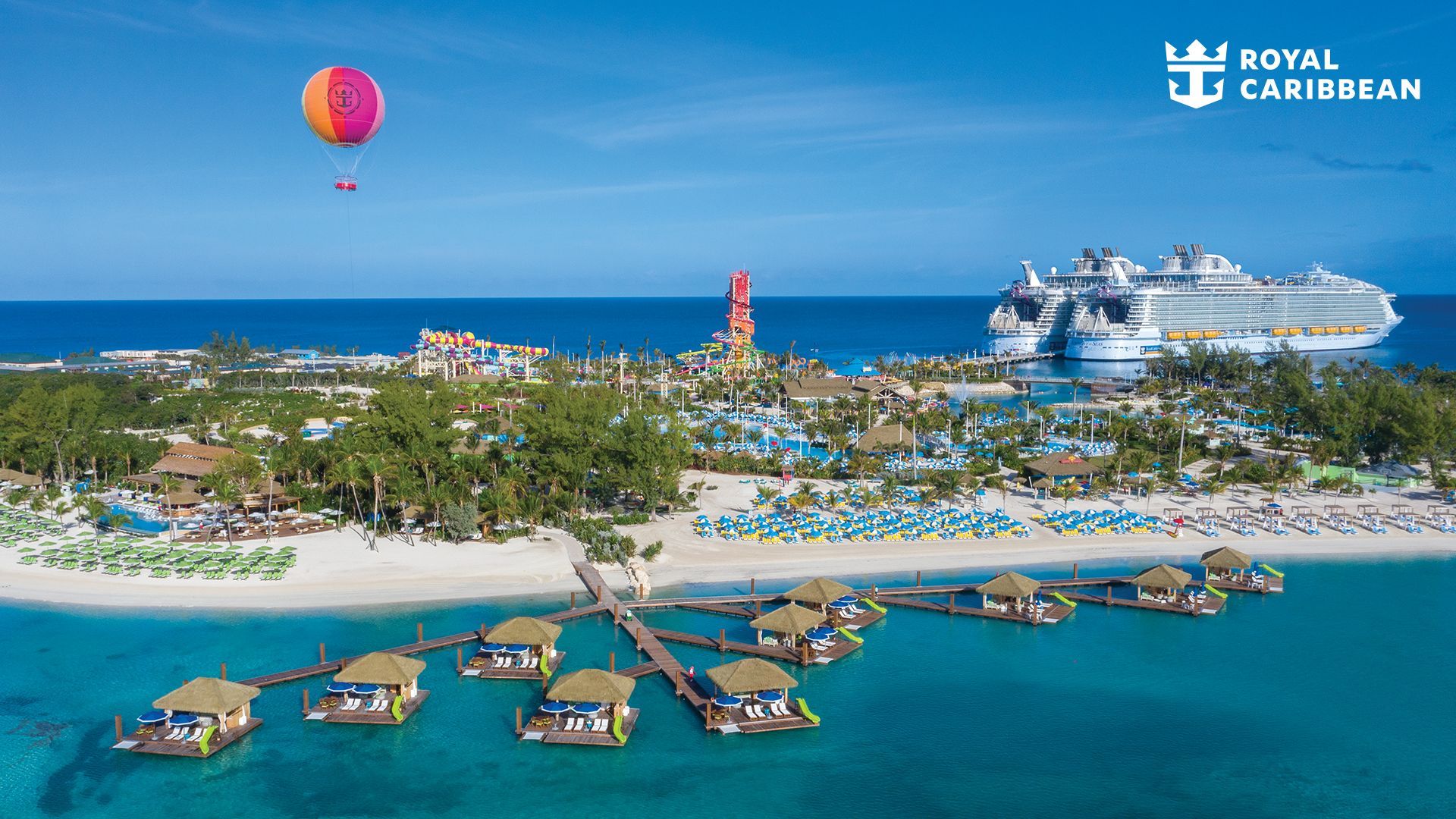 Aerial view of a tropical cruise resort with blue water, sandy beach, overwater huts, and a hot air balloon
