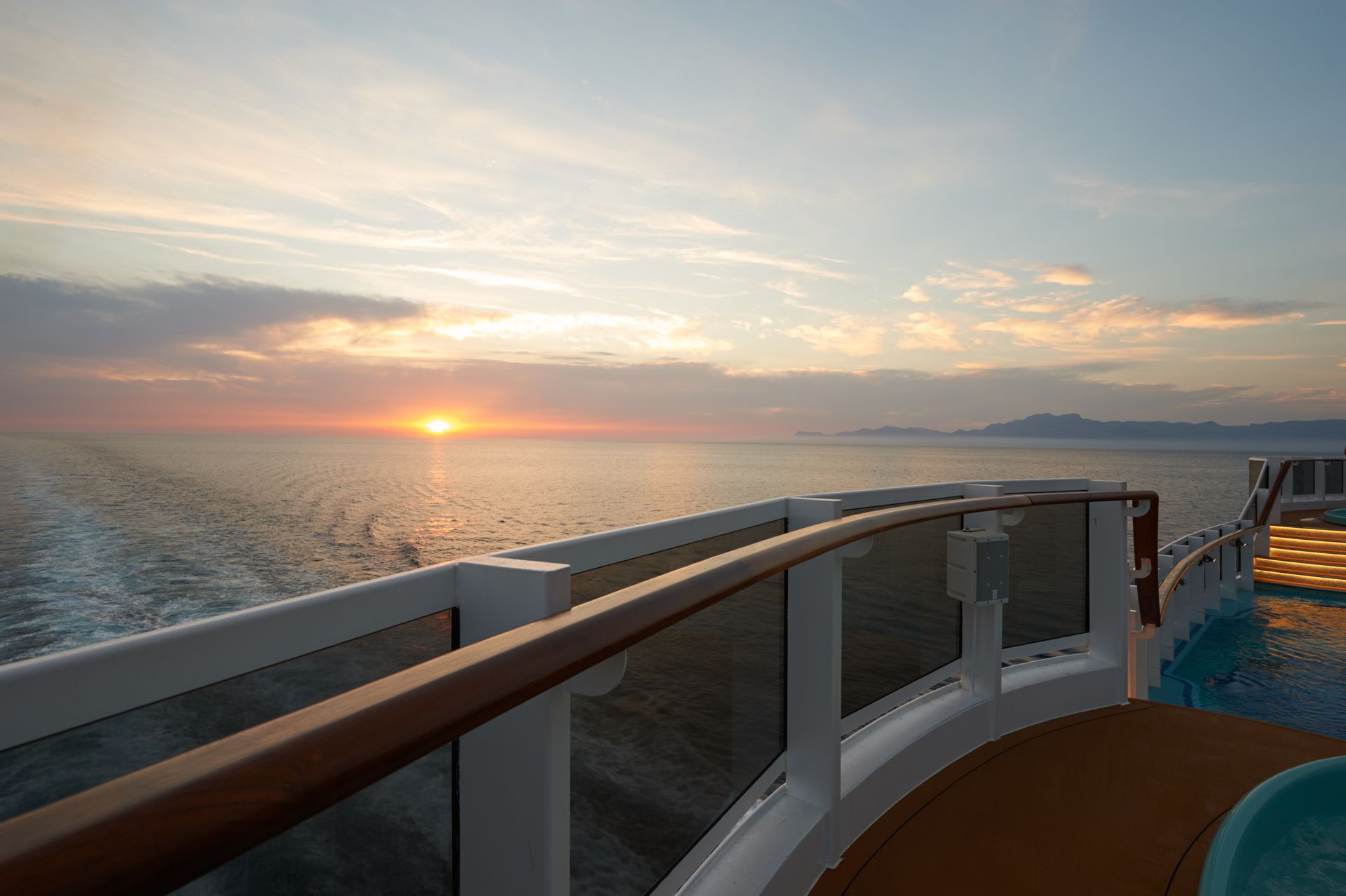 Sunset over the ocean, viewed from a cruise ship deck. Sky is orange and blue.